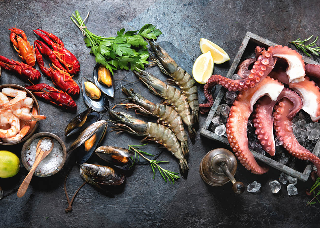 Variety of fresh delicious seafood. Octopus tentacles, black tiger shrimps, king prawn and mussels with fresh herbs and seasoning on black rustic background