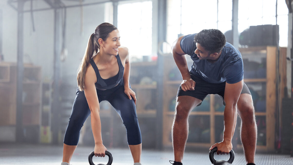 Strong, wellness couple doing kettlebell weight exercise, workout or training inside a gym. Happy sports people or trainer motivation, exercising with fitness equipment for muscle, strength or health