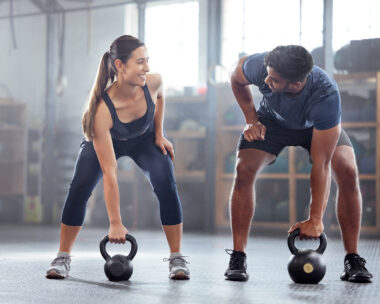 Strong, wellness couple doing kettlebell weight exercise, workout or training inside a gym. Happy sports people or trainer motivation, exercising with fitness equipment for muscle, strength or health