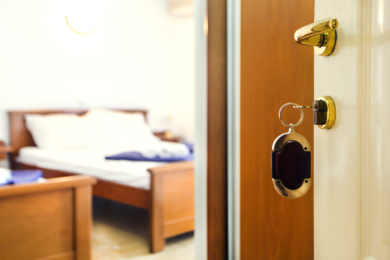 Key in keyhole with bedroom in the background in a hotel or apartment (travel or real estate concept)