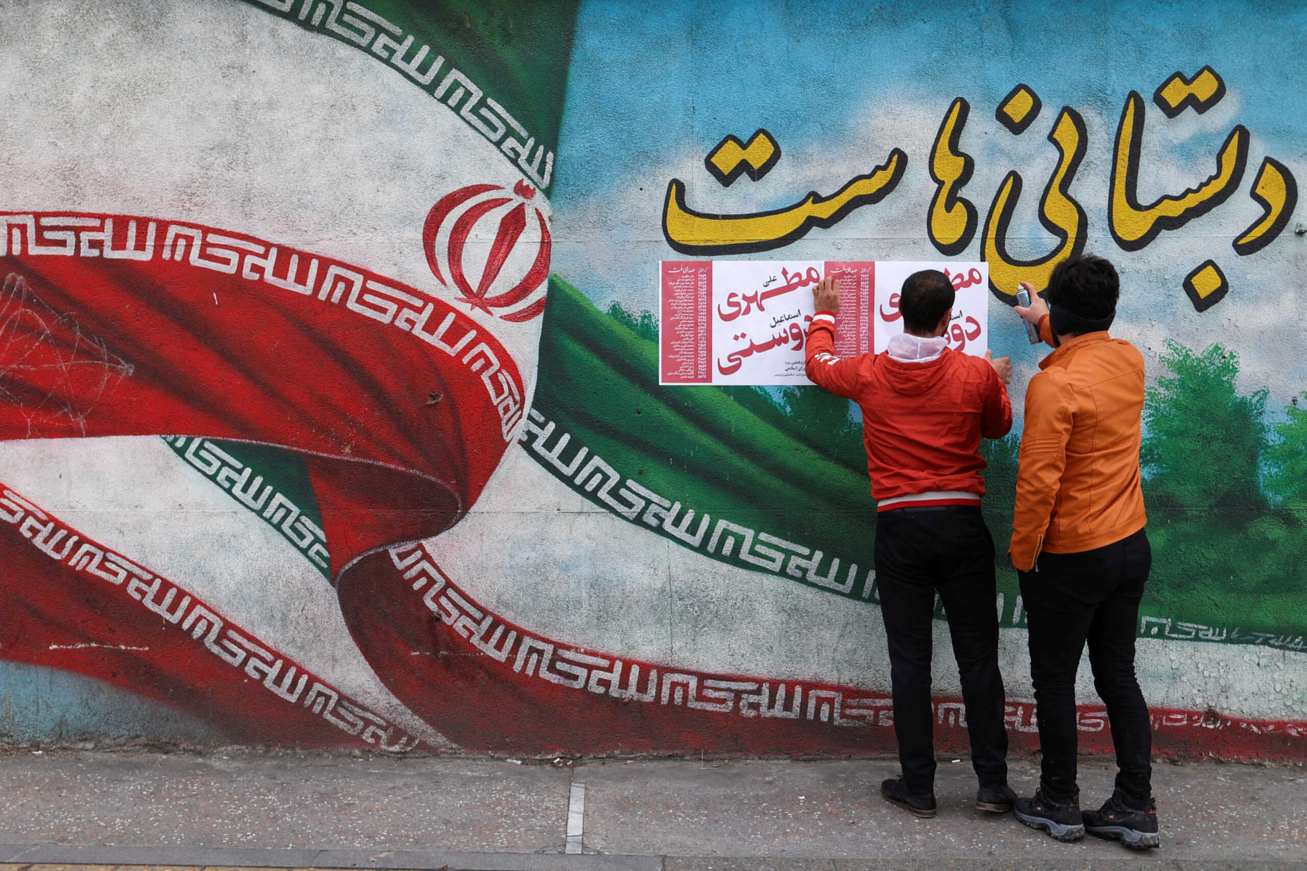 FILE PHOTO: Iranian men put campaign posters on a wall during the last day of election campaigning in Tehran, Iran, February 28, 2024. Majid Asgaripour