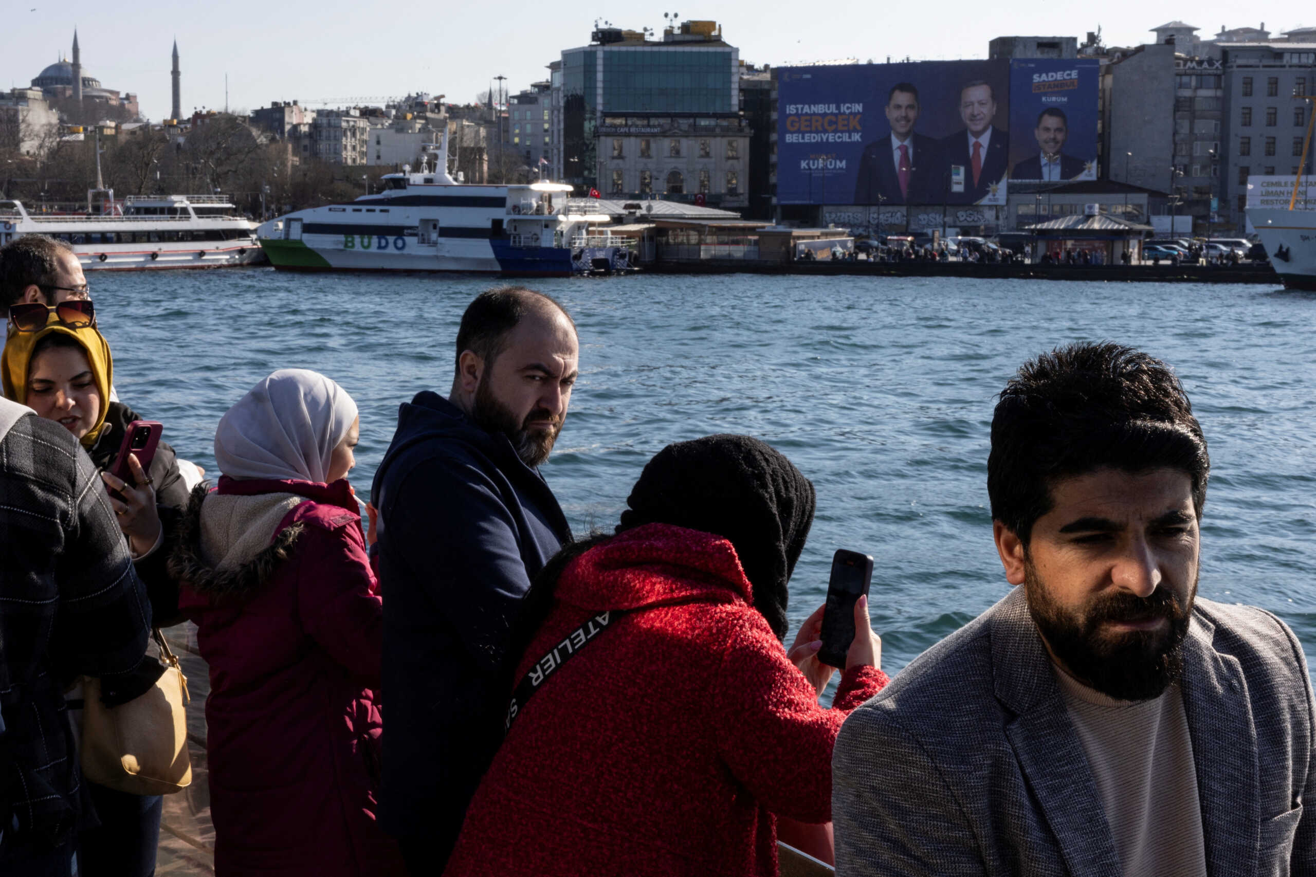 Commuters and tourists on a ferry travel through Bosphorus as election posters for Turkey's President Tayyip Erdogan and mayoral candidate of Istanbul from his ruling AK Party (AKP) Murat Kurum are seen on a building at the background, in Istanbul, Turkey, February 20, 2024. REUTERS