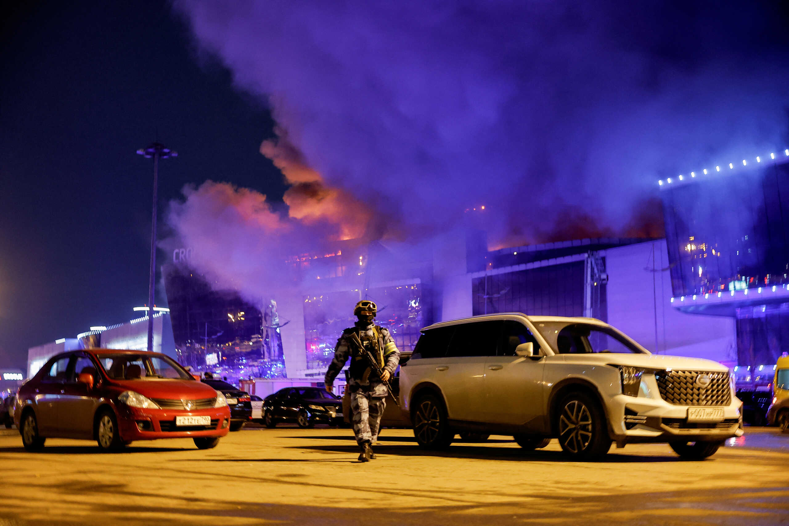 A Russian law enforcement officer walks at a parking area near the burning Crocus City Hall concert venue following a shooting incident, outside Moscow, Russia, March 22, 2024. REUTERS