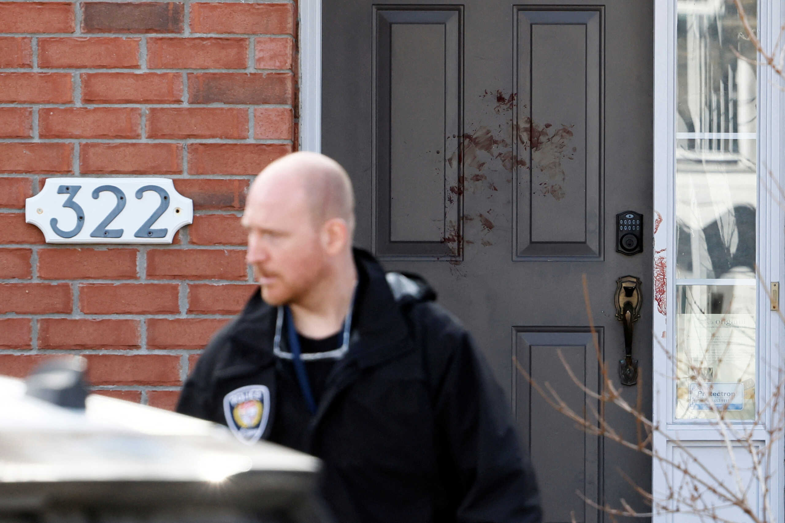 An emergency responder stands near a door smeared in blood after four children and two adults were found dead inside a neighbouring house in the Ottawa suburb of Barrhaven, Ontario, Canada March 7, 2024.  REUTERS