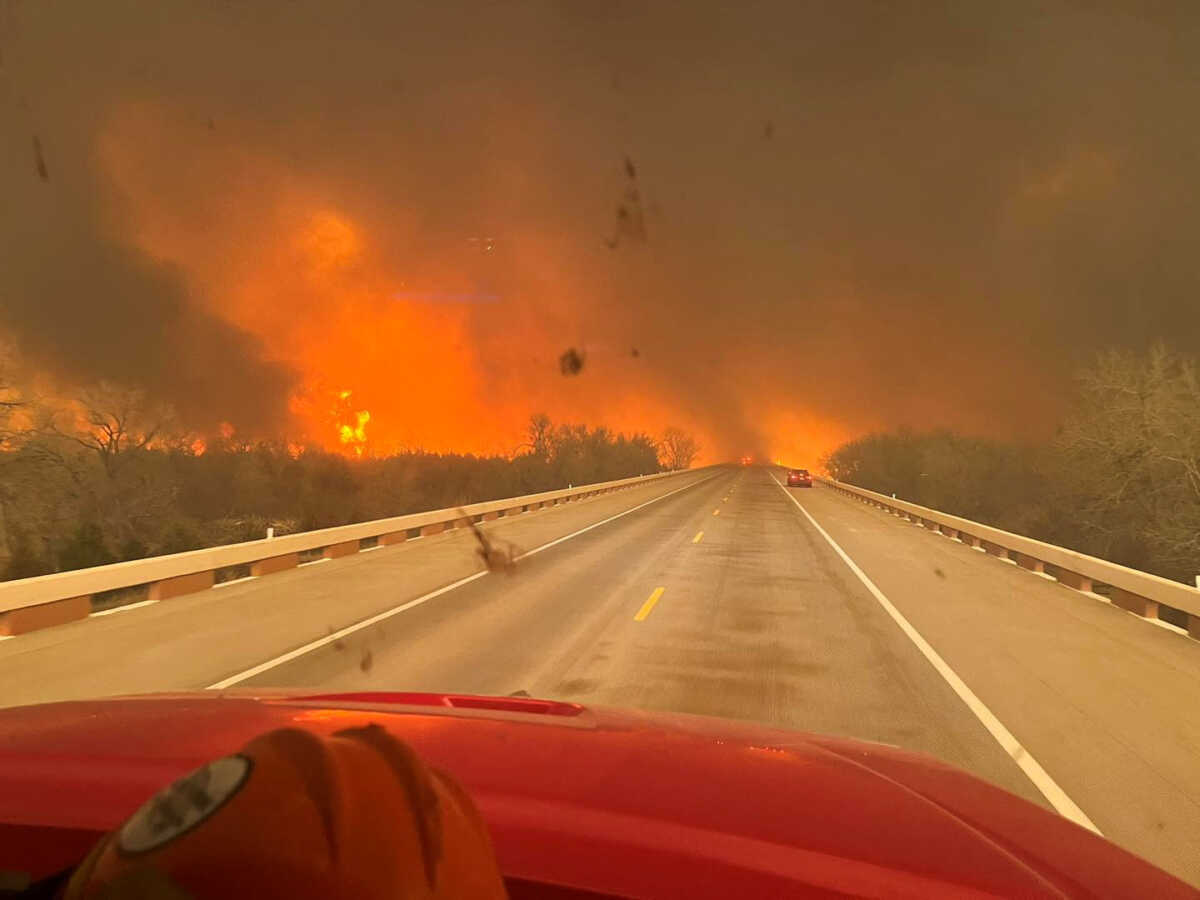 Cars drive as smoke and fire rise from wildfires in a location given as Texas, U.S., in this handout picture released on February 27, 2024. Greenville Fire-Rescue