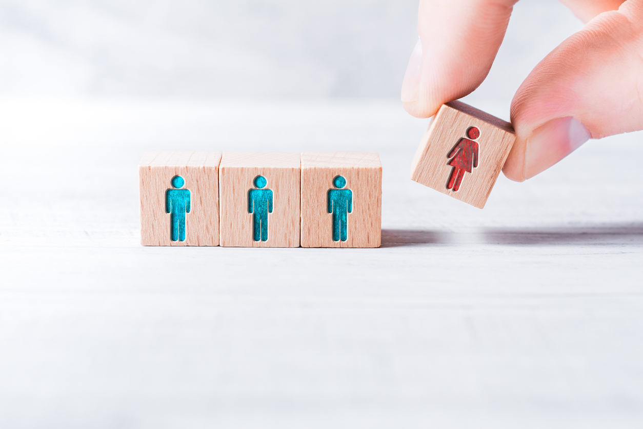 Male Fingers Adding A Block With A Different Colored Female Icon To 3 Blocks With Equal Colored Man Icons On Table - Gender Equality Concept