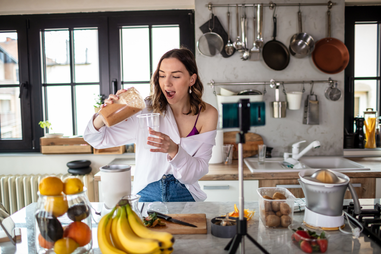 Photo of young woman in kitchen live streaming about healthy food.
