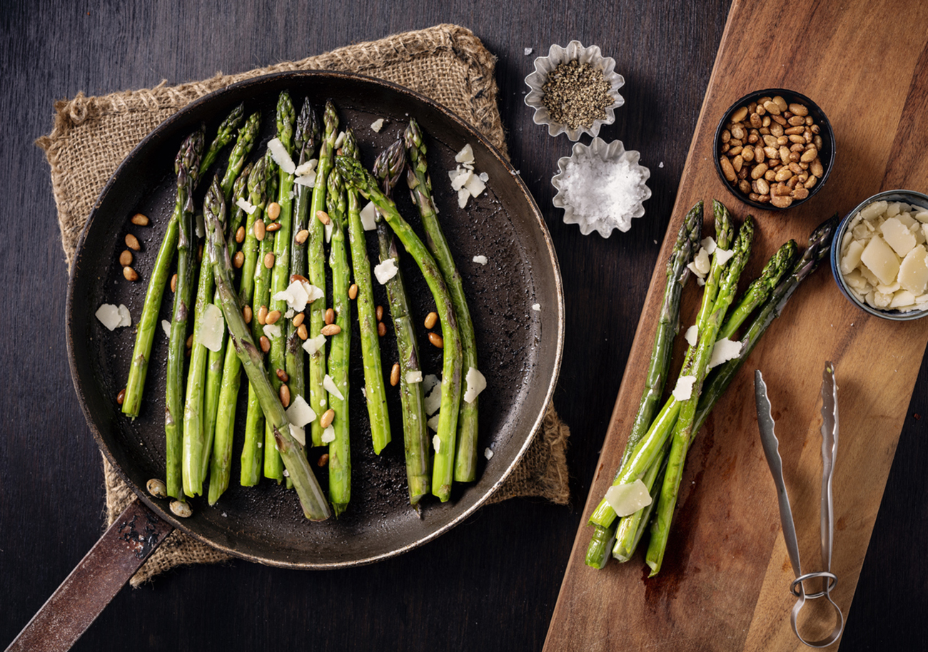 Pan fried asparagus served from the skillet. Cooked with a tiny bit of oil or butter just give a bit of colour and taste to the asparagus stems. Served with; pine nuts, vegan parmesan cheese and salt and pepper.Overhead view, horizontal format with some copy space.