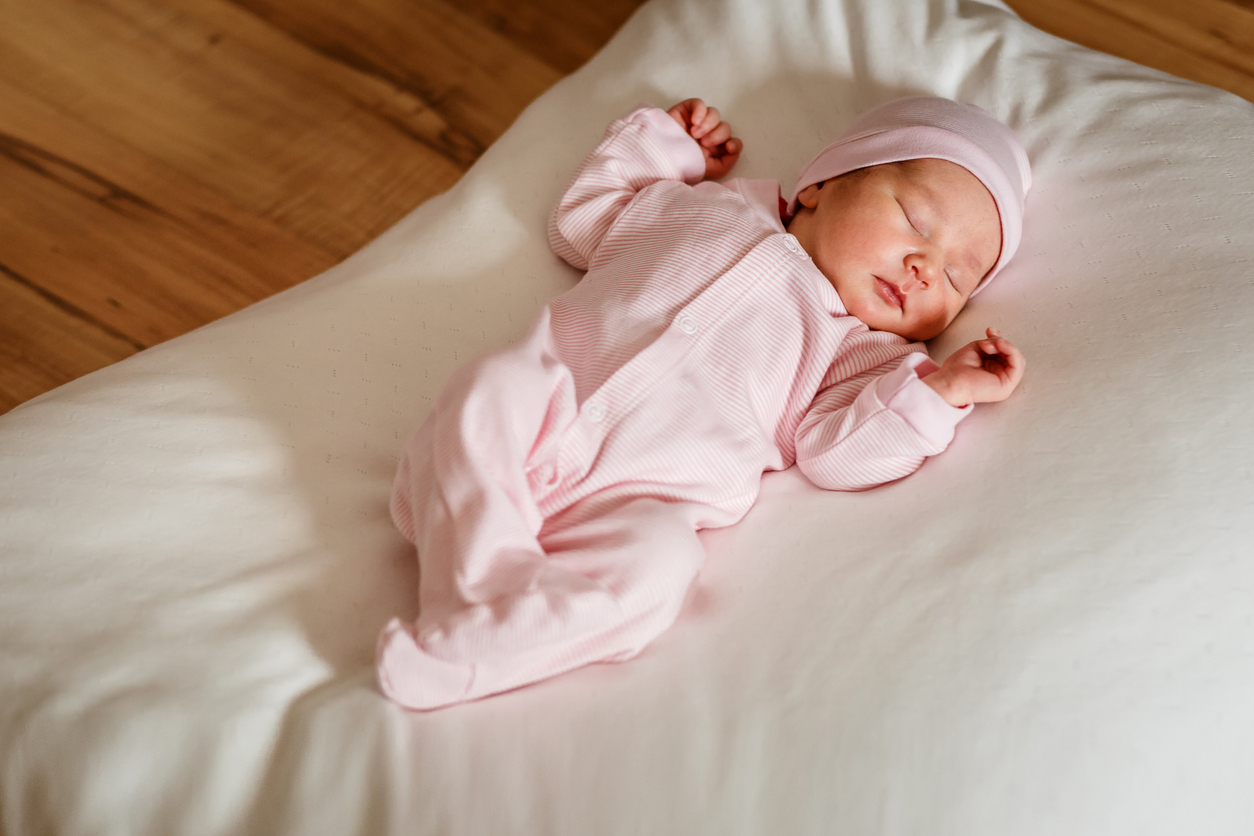 Cute little newborn baby girl of one week sleeps sweetly on a white blanket in natural light