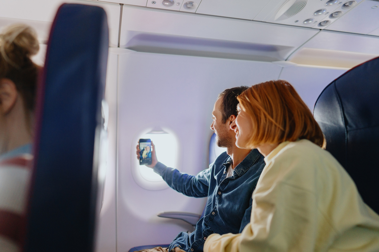 Photo of a young couple taking selfies while traveling by plane.