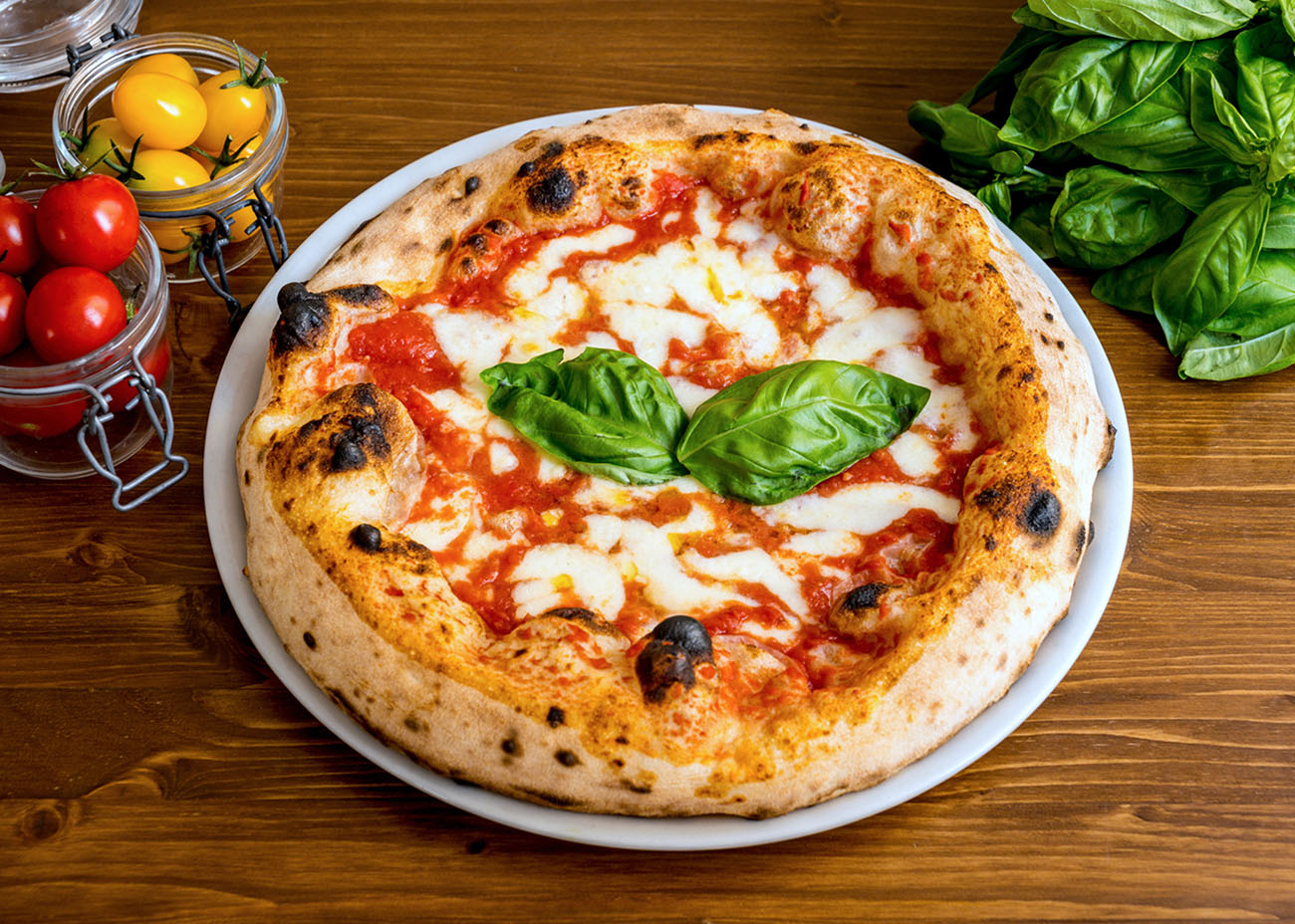 A delicious and tasty Italian pizza Margherita with fresh tomatoes, buffalo mozzarella and extra virgin olive oil, strictly cooked in a wood oven, according to the original tradition of Naples. In 2017 the art of Neapolitan pizza was declared by UNESCO as an Intangible Cultural Heritage. Image in High Definition format.