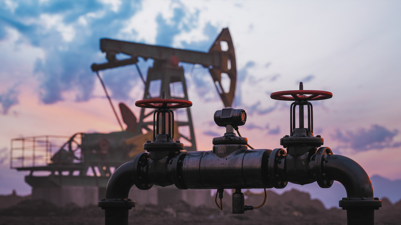 Gas pipe and pump jack silhouette against a sunset sky.