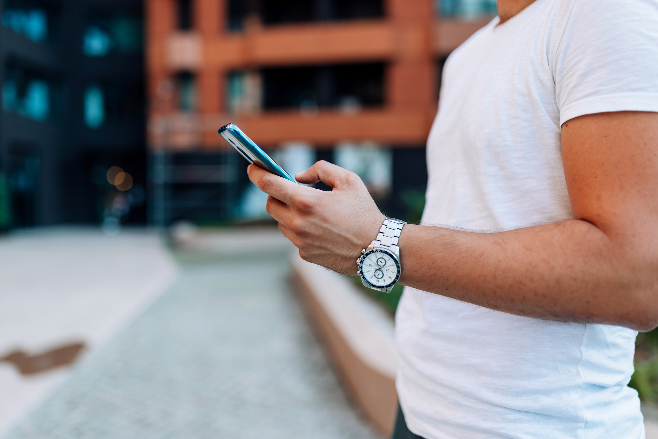 A close-up of a young Caucasian man holding a cellphone, while standing outside.