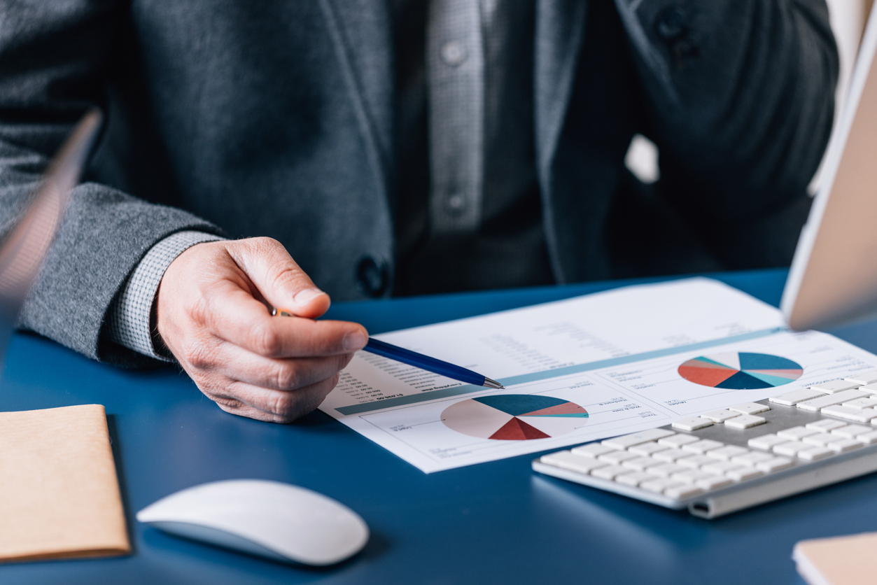 Businessperson reviewing pie charts and data analysis documents in an office setting.