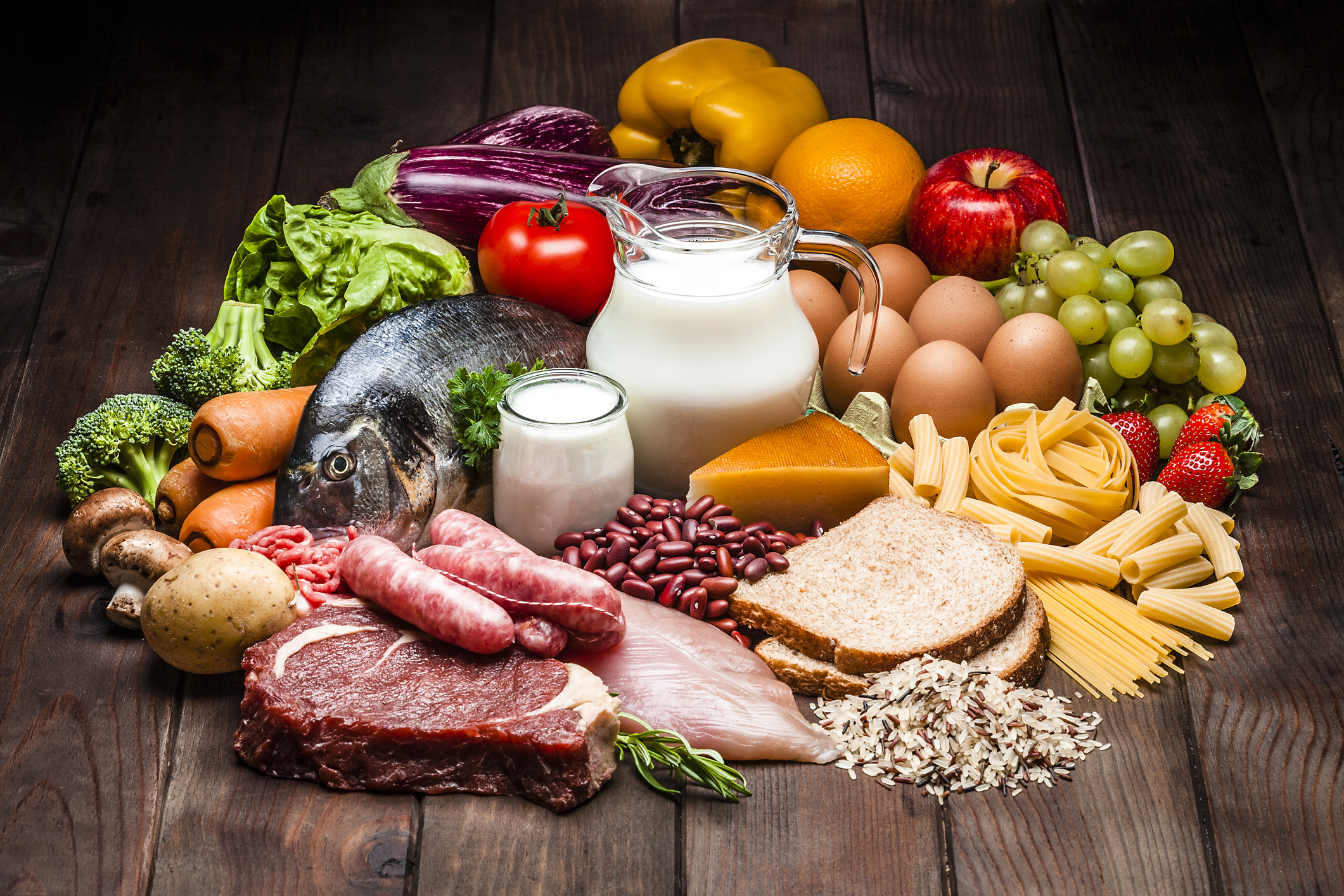 Large group of different types of food like carbohydrates, protein and dietary fiber shot on rustic wooden table. Food included in the composition are dairy products, sausages, minced meat, fish, bread, pasta, beans, fruits and vegetables. DSRL studio photo taken with Canon EOS 5D Mk II and Canon EF 70-200mm f