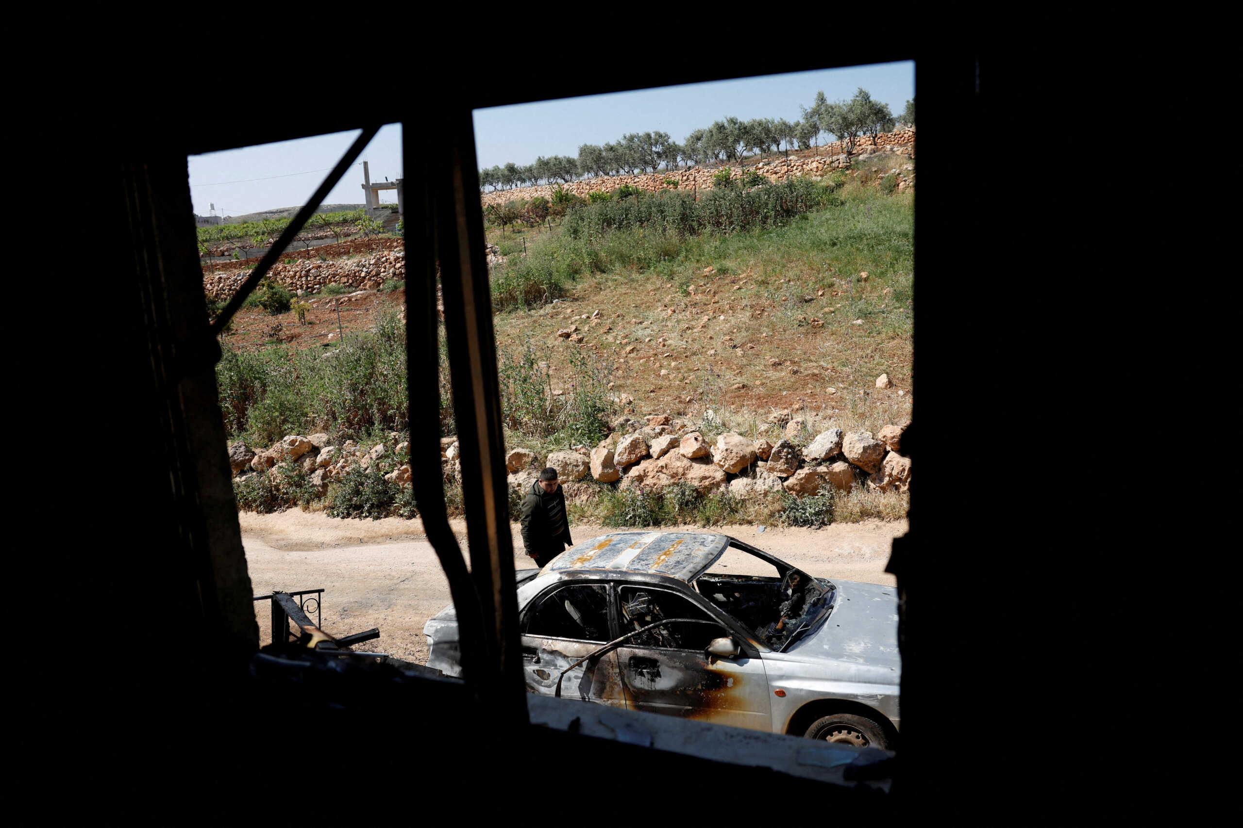 A Palestinian man inspects the damage to a car after Israeli settlers attacked the village of al-Mughayyer, in the Israeli-occupied West Bank, April 13, 2024. REUTERS