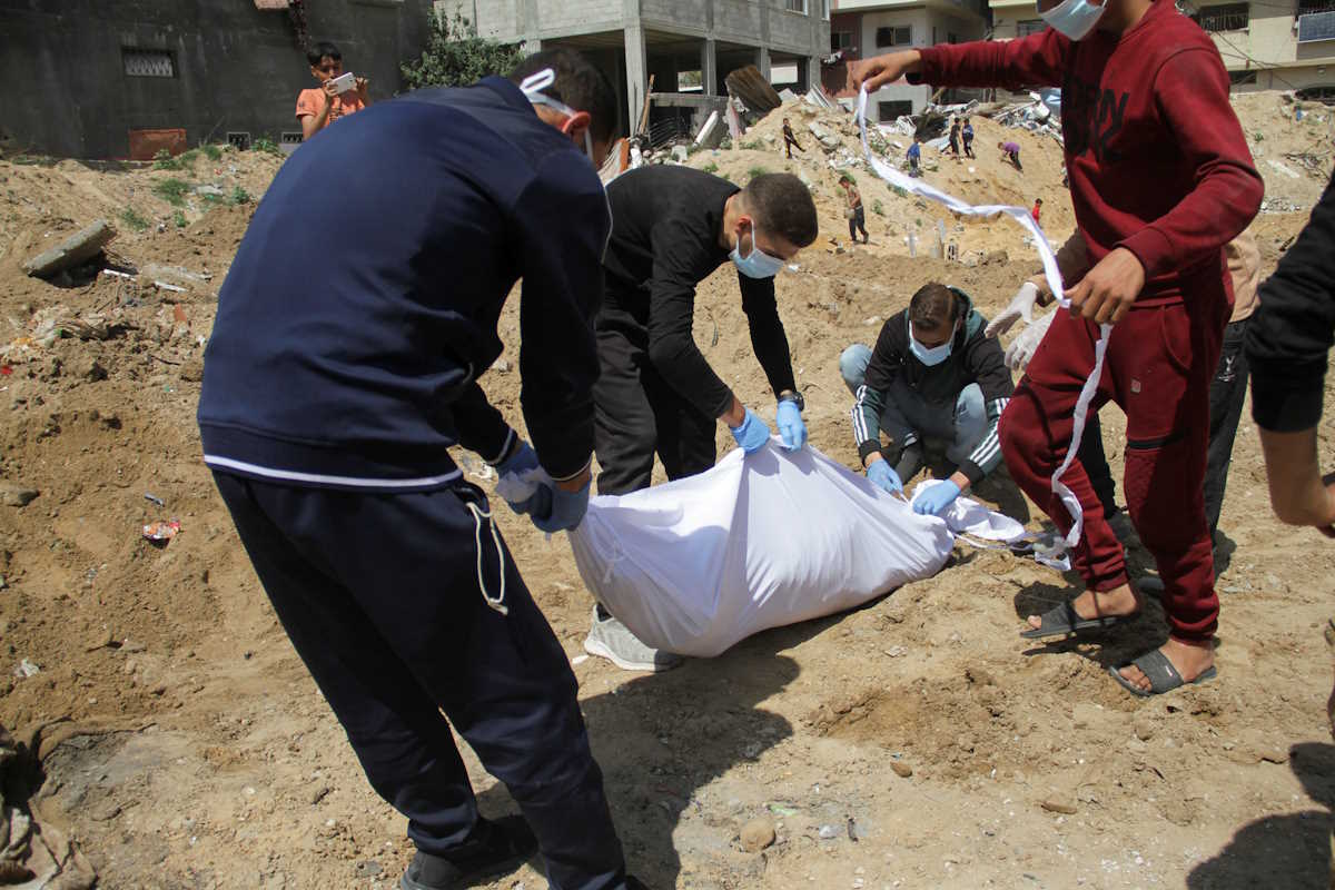 Palestinians cover a body, which was buried in a mass grave, amid the ongoing conflict between Israel and Hamas, in northern Gaza Strip, April 15, 2024. REUTERS