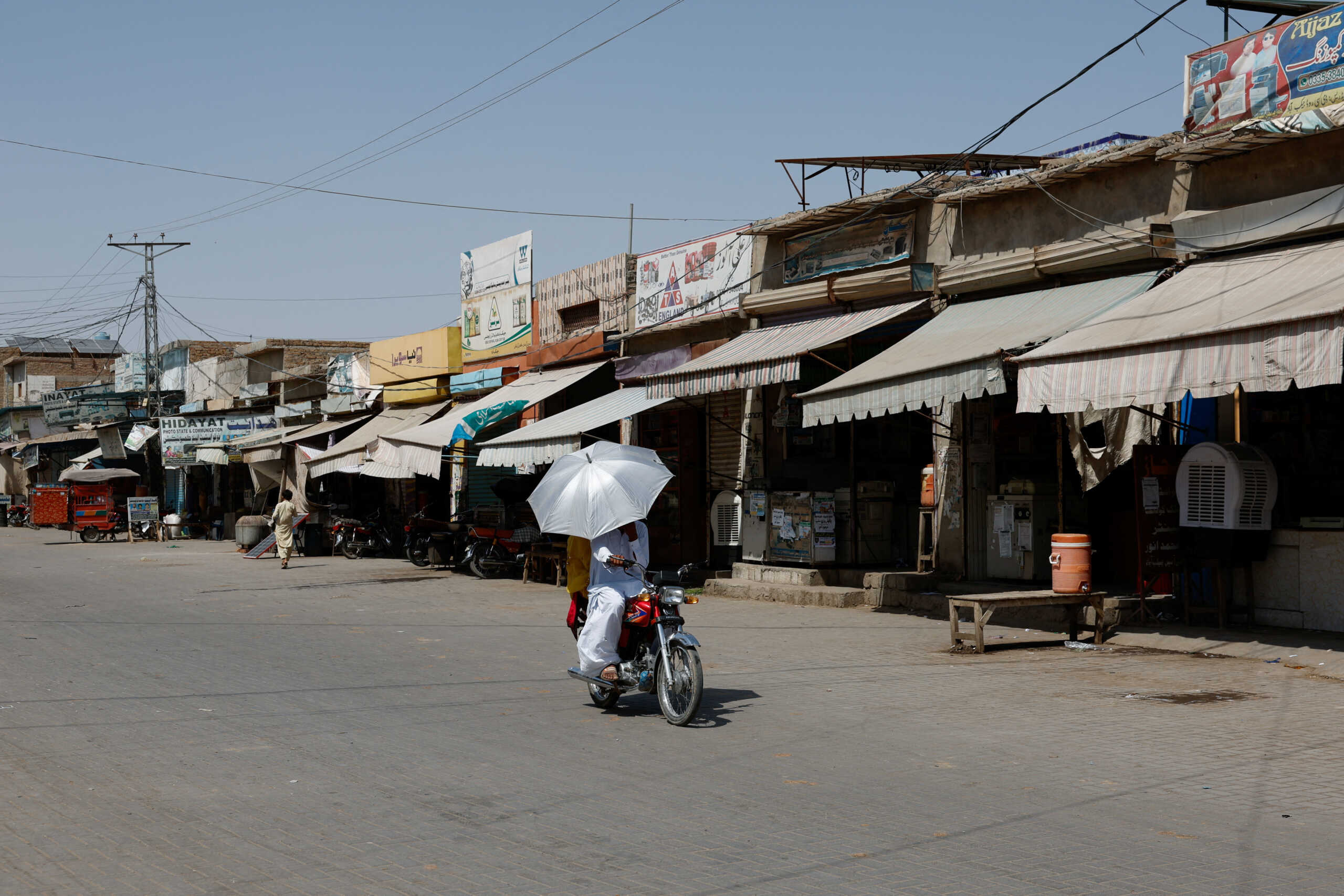 A couple rides on a motorbike carrying an umbrella to avoid sunlight, along a deserted market during a hot summer day as the heatwave continues in Jacobabad, Pakistan May 26, 2024. REUTERS
