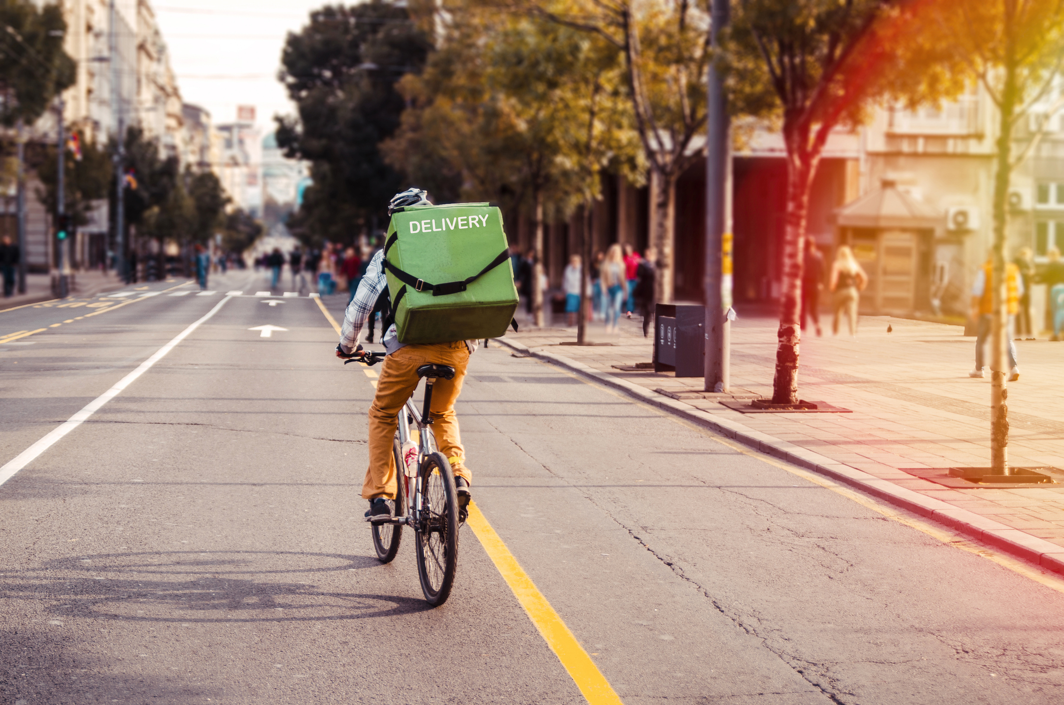 Delivery man food service courier on bicycle in town. Rear view of man riding a bicycle in the city street with green bag on back