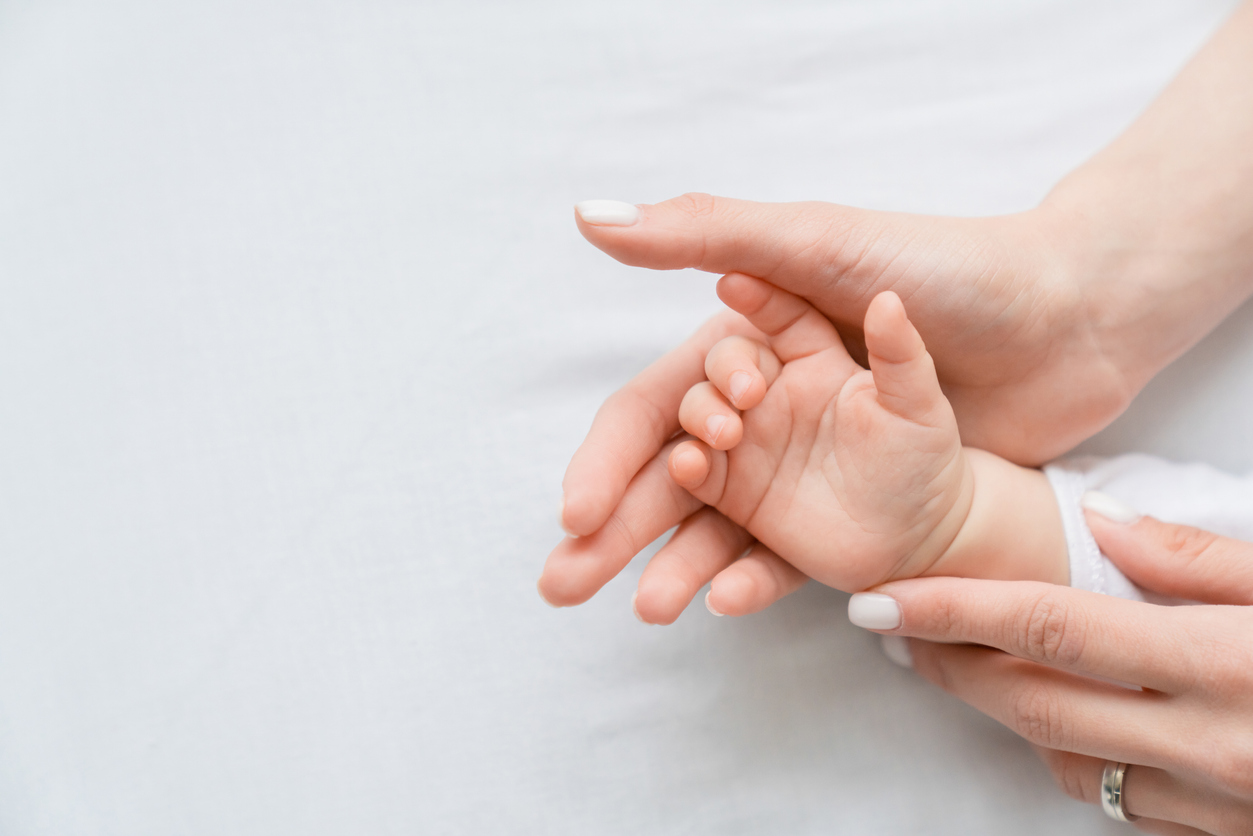 Close up image of a mother`s mom hand holding her little small toddler`s infant newborn tiny hand on white background. Childcare, motherhood concept.