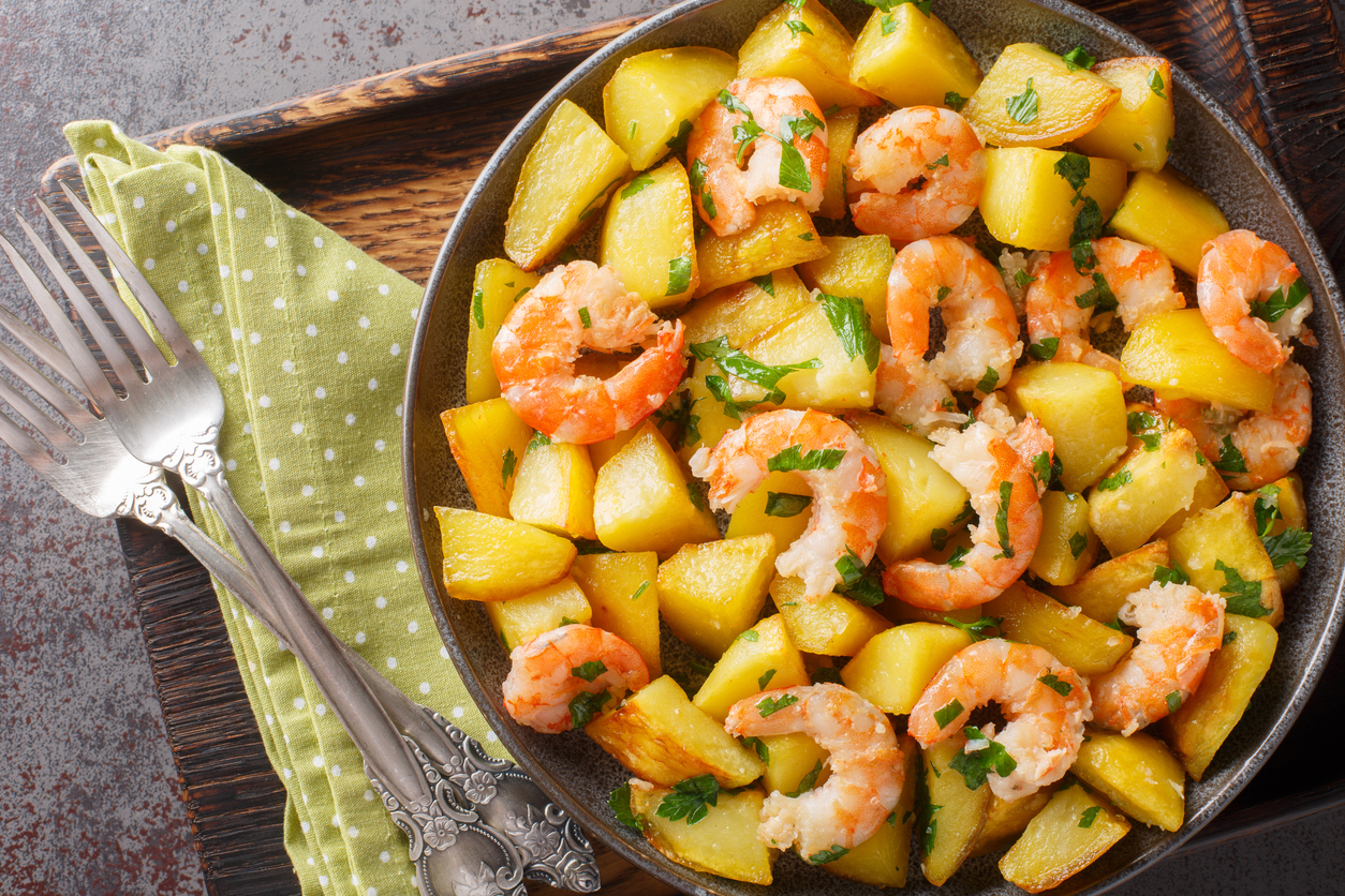 Potatoes sauteed with shrimp and garlic close-up in a plate on the table. Horizontal top view from above