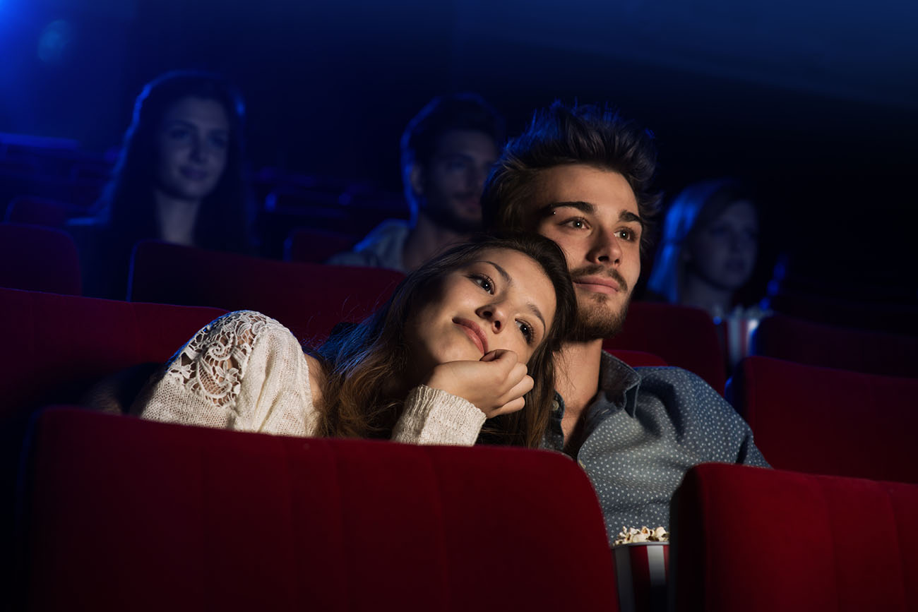 Young loving couple at the cinema watching a movie, he is hugging her girlfriend
