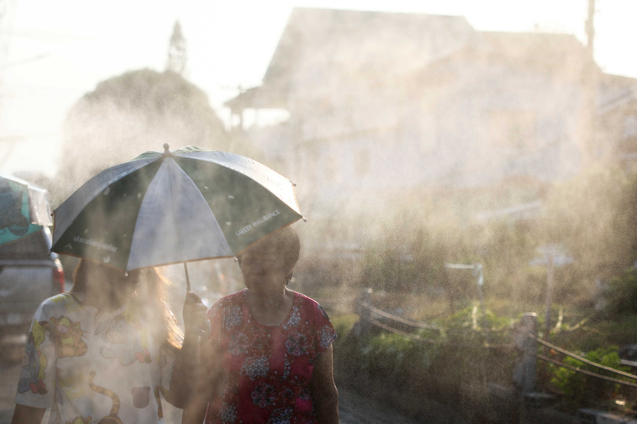 People walk with an umbrella through sprinkling water as Thai authorities said that people were dying from heat stroke this year and warned to avoid outdoor activities, in Bangkok, Thailand, May 5, 2024. REUTERS