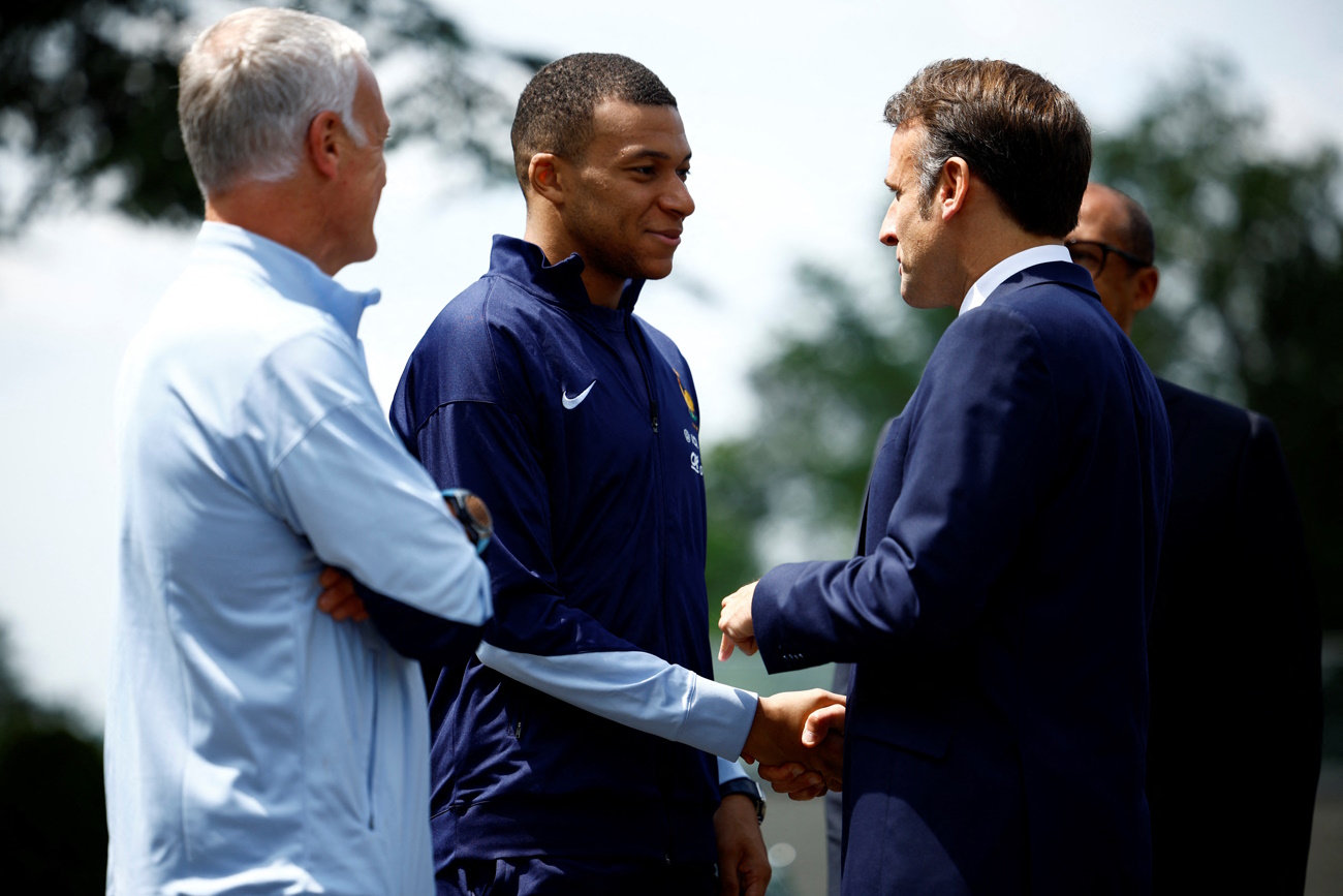 French President Emmanuel Macron shakes hands with French player Kylian Mbappe, next to Didier Deschamps, coach of French national football team,  as he arrives for a lunch at their training camp ahead of the UEFA Euro 2024, in Clairefontaine-en-Yvelines, France, June 3, 2024. REUTERS