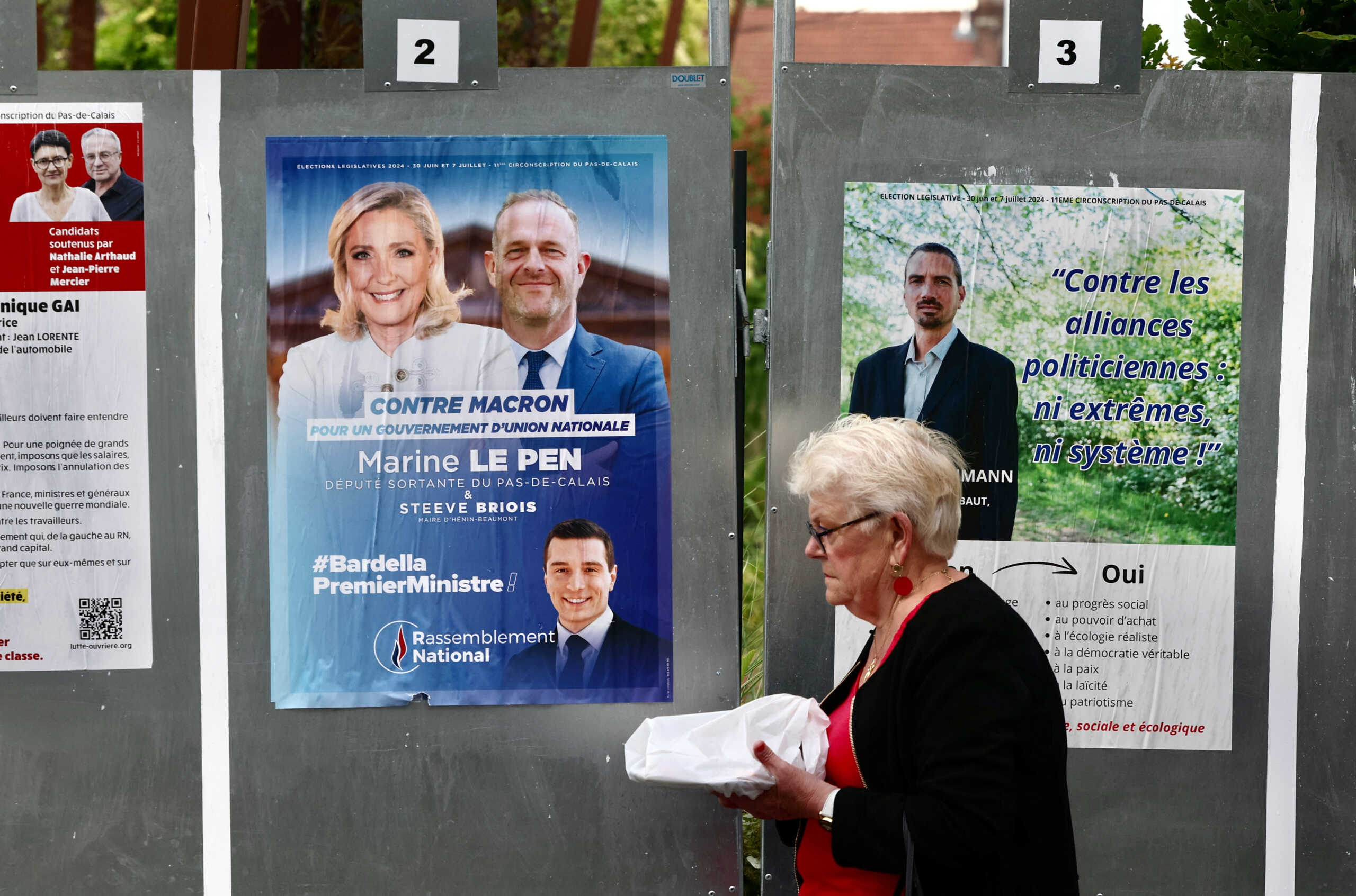 A woman walks past election boards with a campaign poster of French far-right Rassemblement National (National Rally - RN) party with the faces of  RN leader Marine Le Pen and RN President Jordan Bardella on the eve of the first round of the early French parliamentary elections, in Henin-Beaumont, France, June 29, 2024. The slogan reads "Bardella Prime Minister". REUTERS