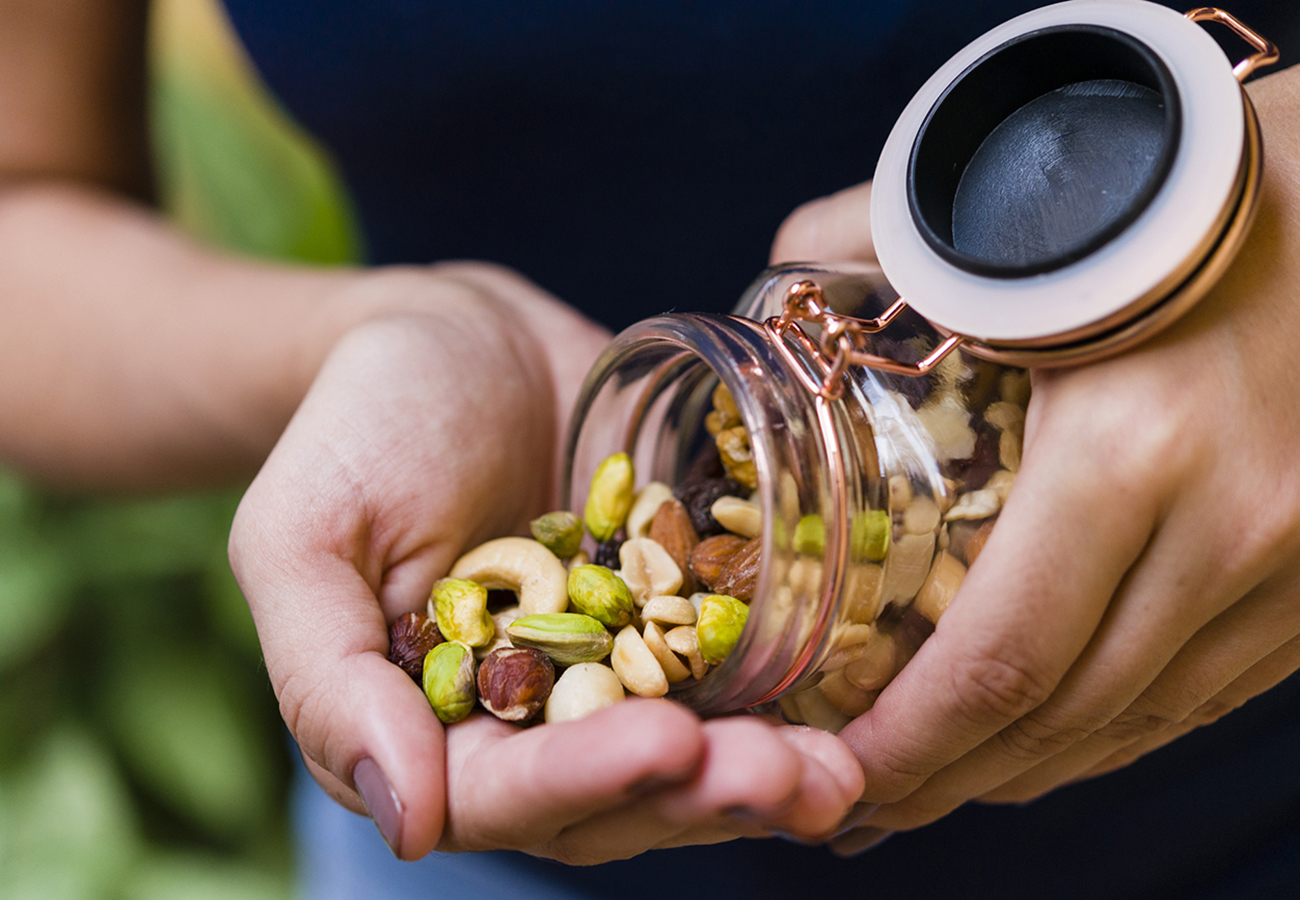 Brunette model hand holding glass hermetic pot with mix of nuts.