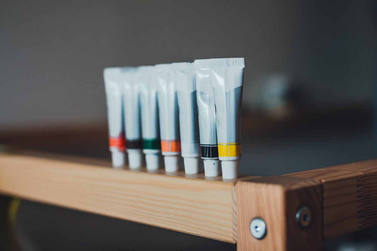 Creative shot - row of acrylic paint tubes on the edge of baby cot. Artist at home
