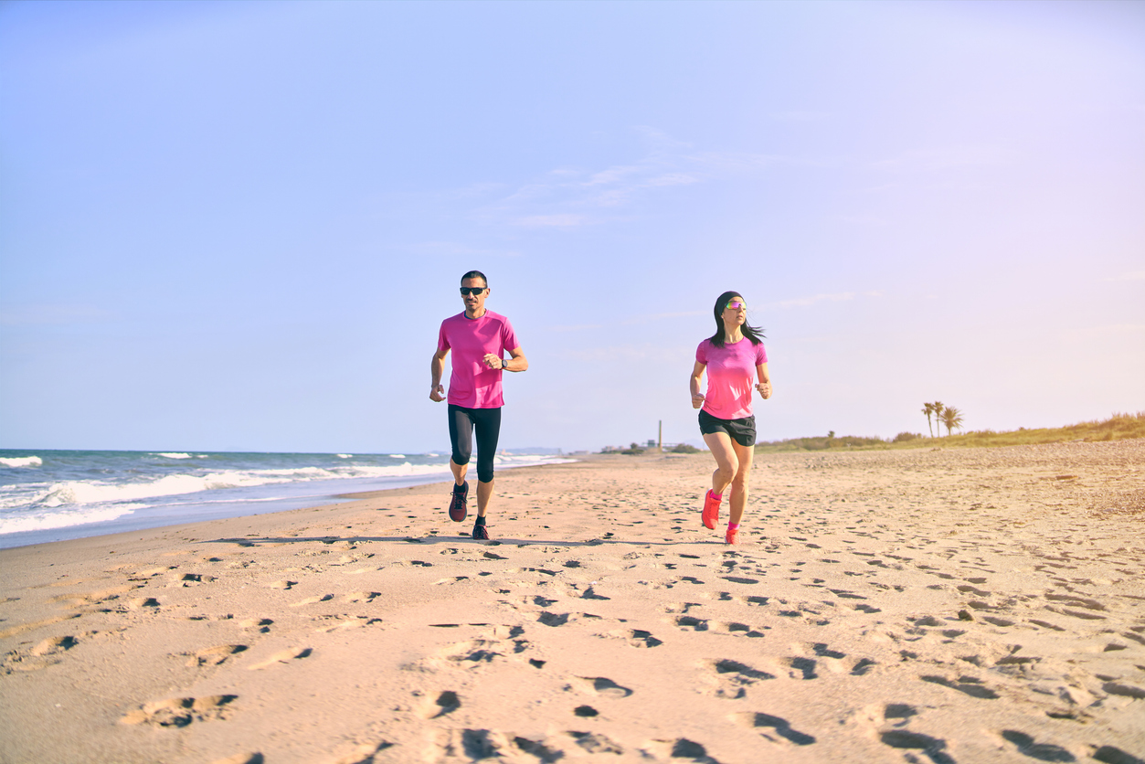 Young fit couple running towards the camera on the beach during sunrise. Healthy start of the day. Wearing pink and black sportswear. Running by the sea.