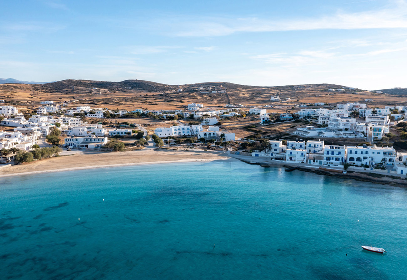 Greece, Koufonisi island, small Cyclades. Aerial drone view. Pano Koufonisi white traditional village buildings, Megali Ammos sandy beach. Calm turquise sea water, clear blue sky background.