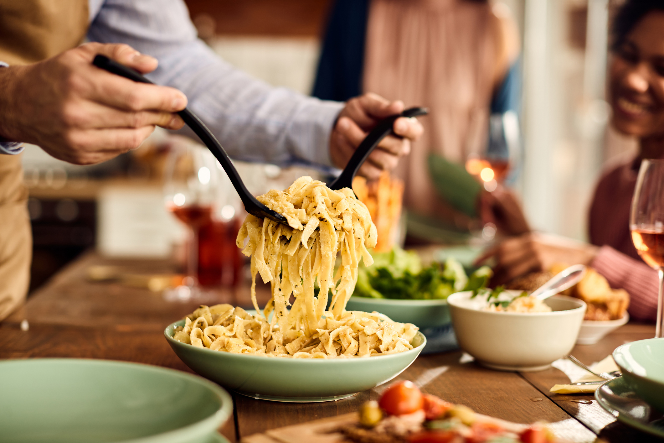 Close-up of man serving pasta to his friends during lunch in dining room.