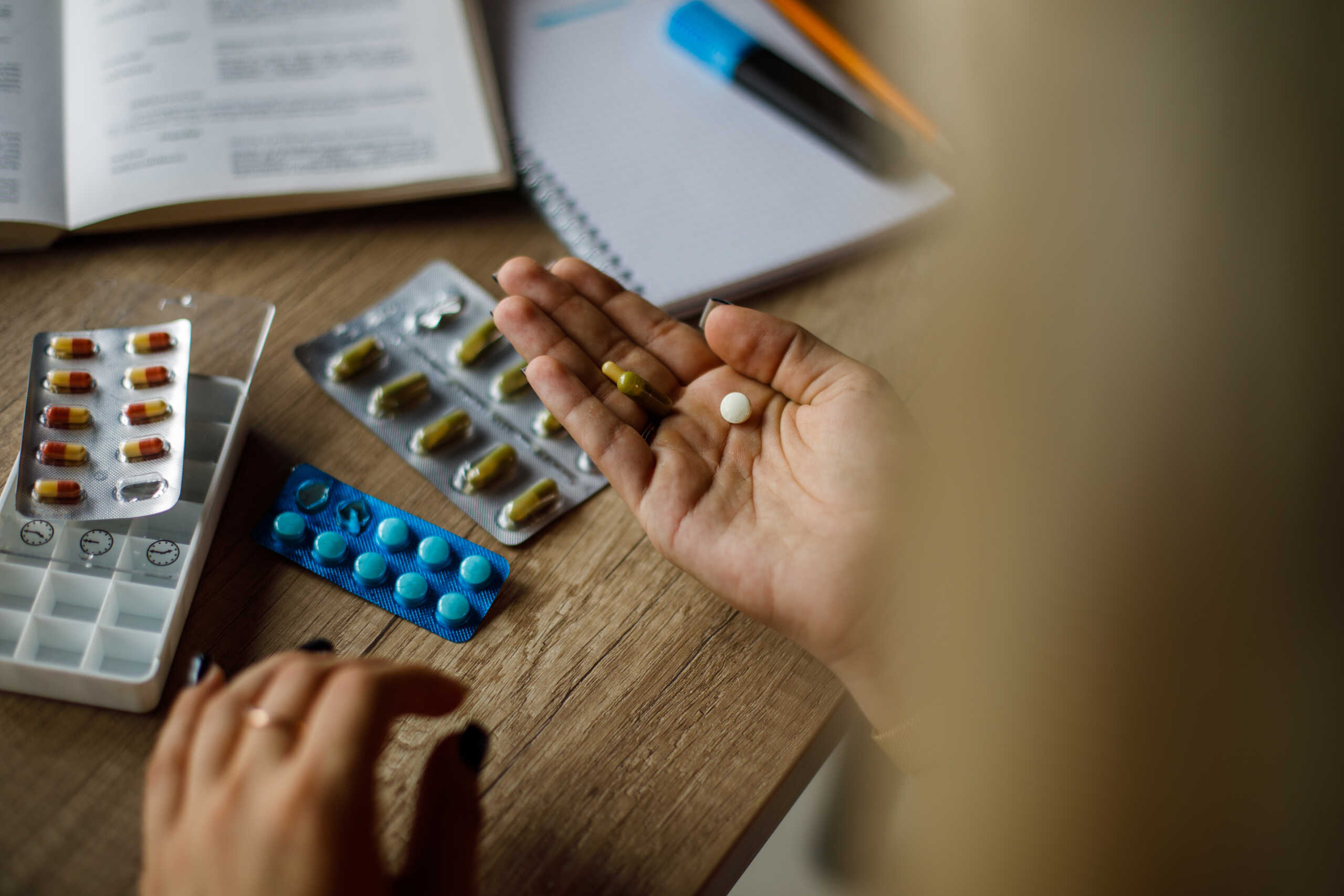 Selective focus shot of unrecognizable woman sitting at her desk, taking pills out of their packages, putting on the palm of her hand, about to arrange them in a pill case organizer.