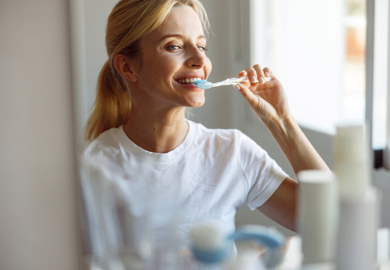 Close up. Cheerful young blonde female brushing teeth with toothbrush at mirror. Take care of teeth.