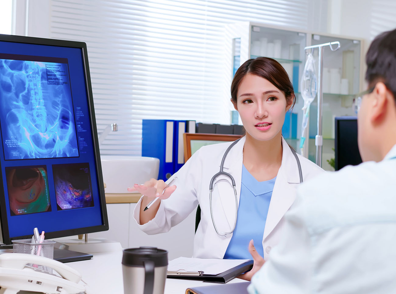 attractive young brunette ponytail female asian doctor wear white coat and stethoscope pen pointing explaining xray film on computer to male patient at clinic