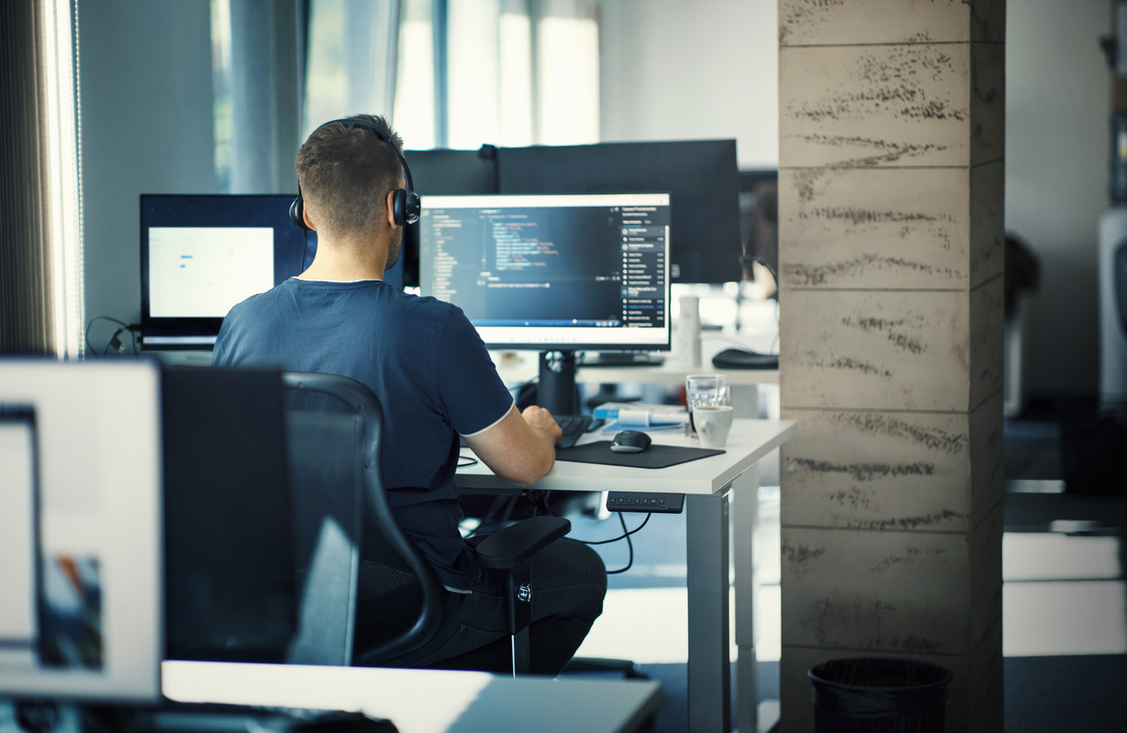 Closeup rear view of a young man coding on multiple computers