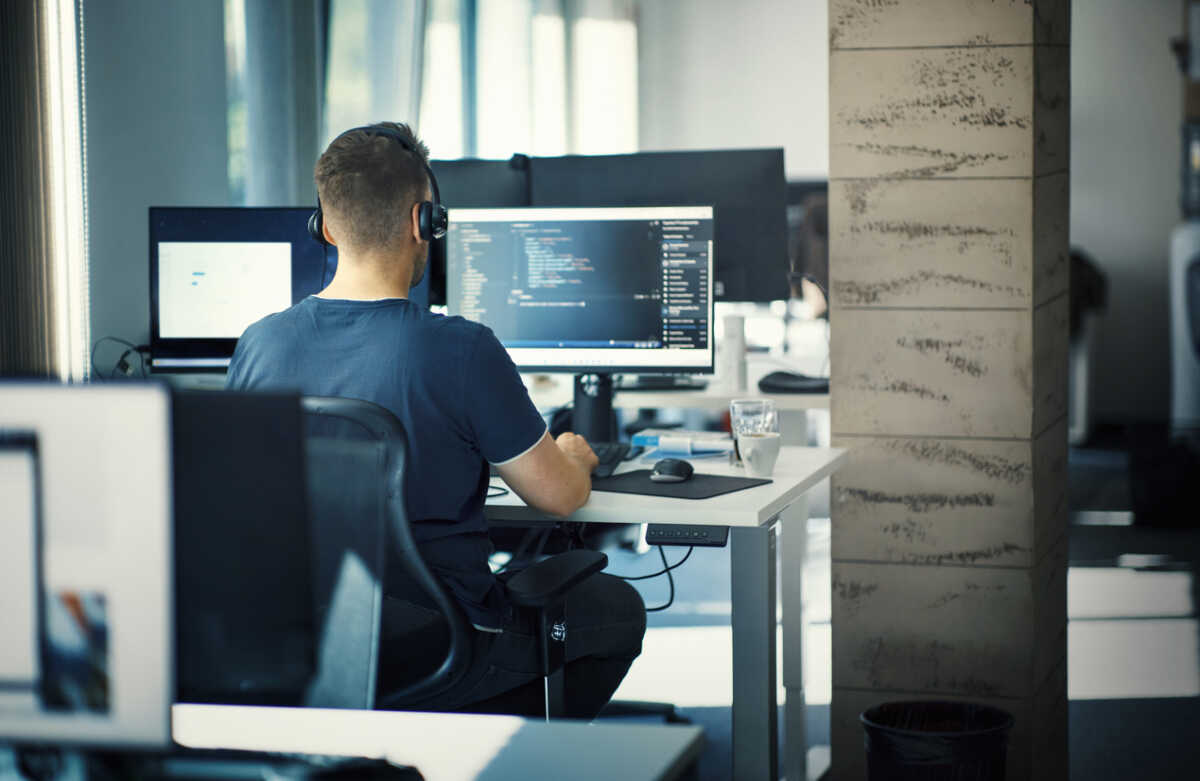 Closeup rear view of a young man coding on multiple computers