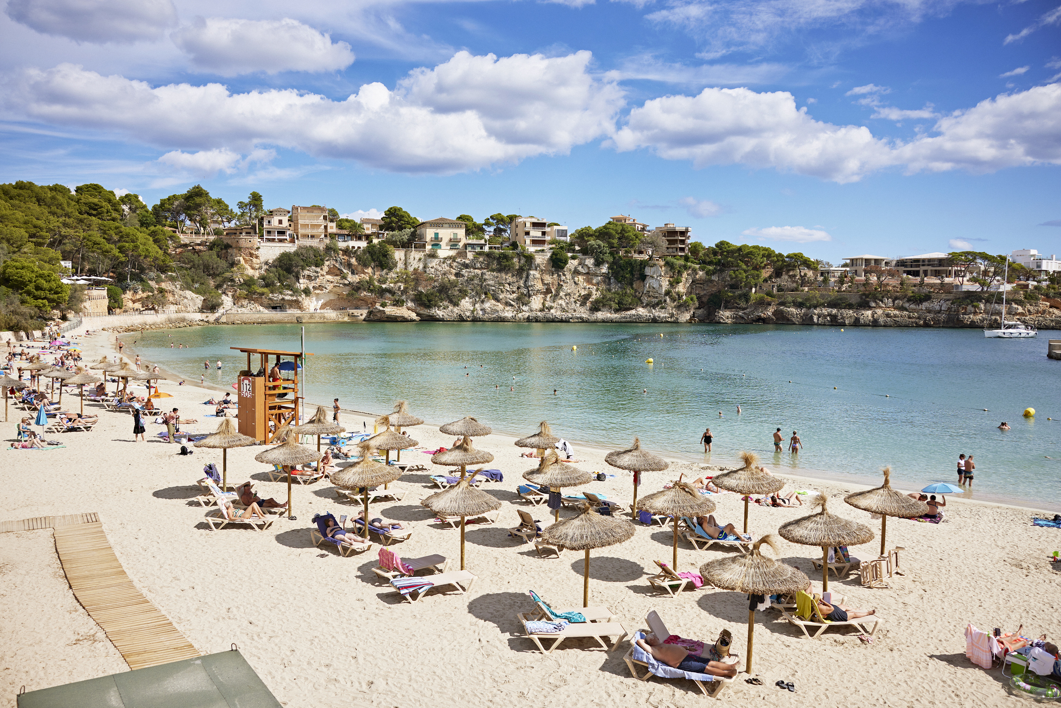 Vacationers relaxing under umbrellas and enjoying calm, crystal clear water of natural inlet. Homes on cliffs in background.