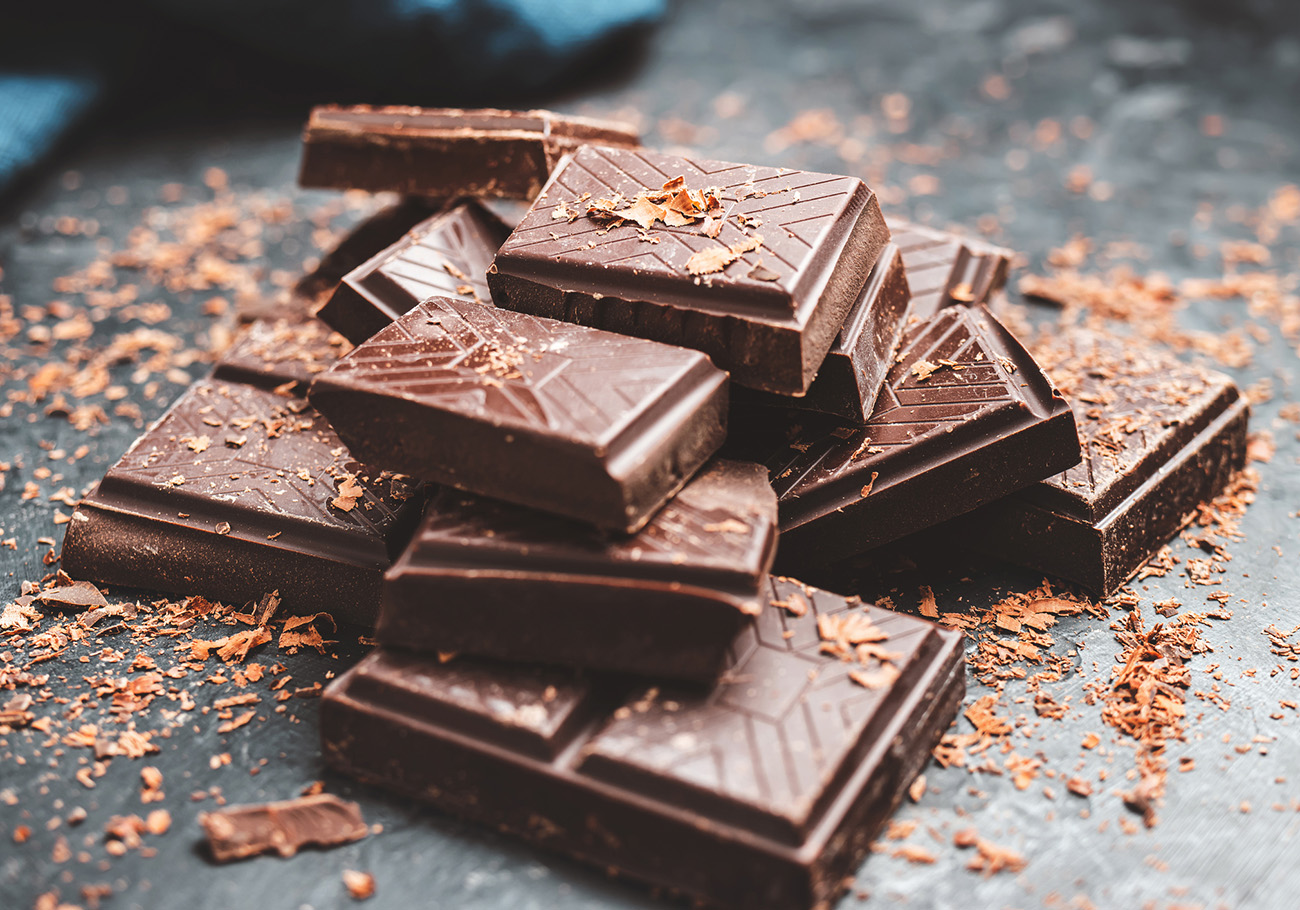 Dark chocolate bar pieces on dark background with grated chocolate, pile chunks of broken chocolate.