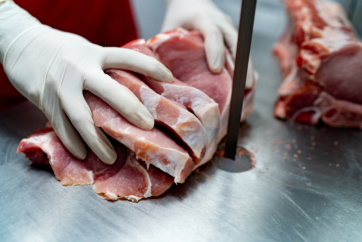 Close up shot of butcher cutting a block of por with an electric saw - People at work concepts