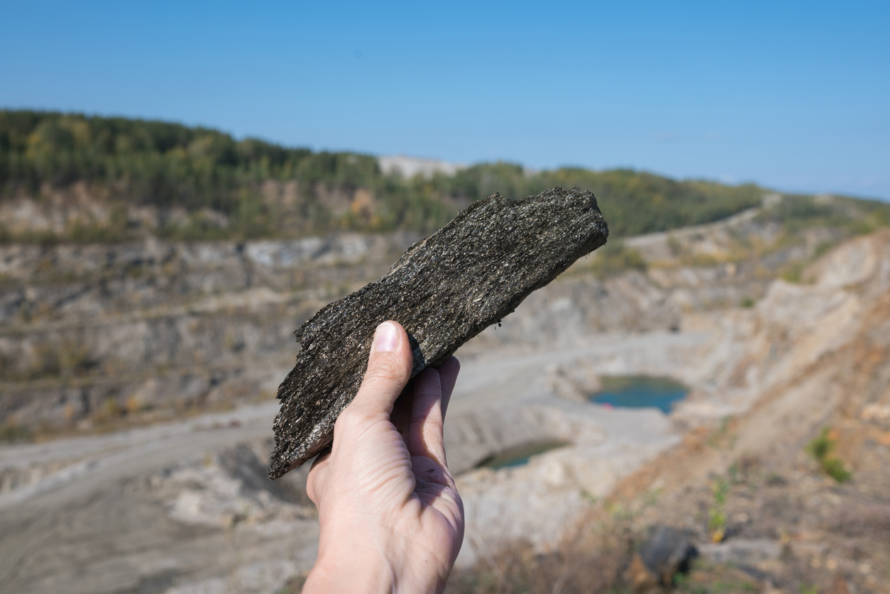 A scenic landscape showing a mining site with a prominent graphite deposit, heavy mineral production equipment, and natural rock formations in the surrounding area.