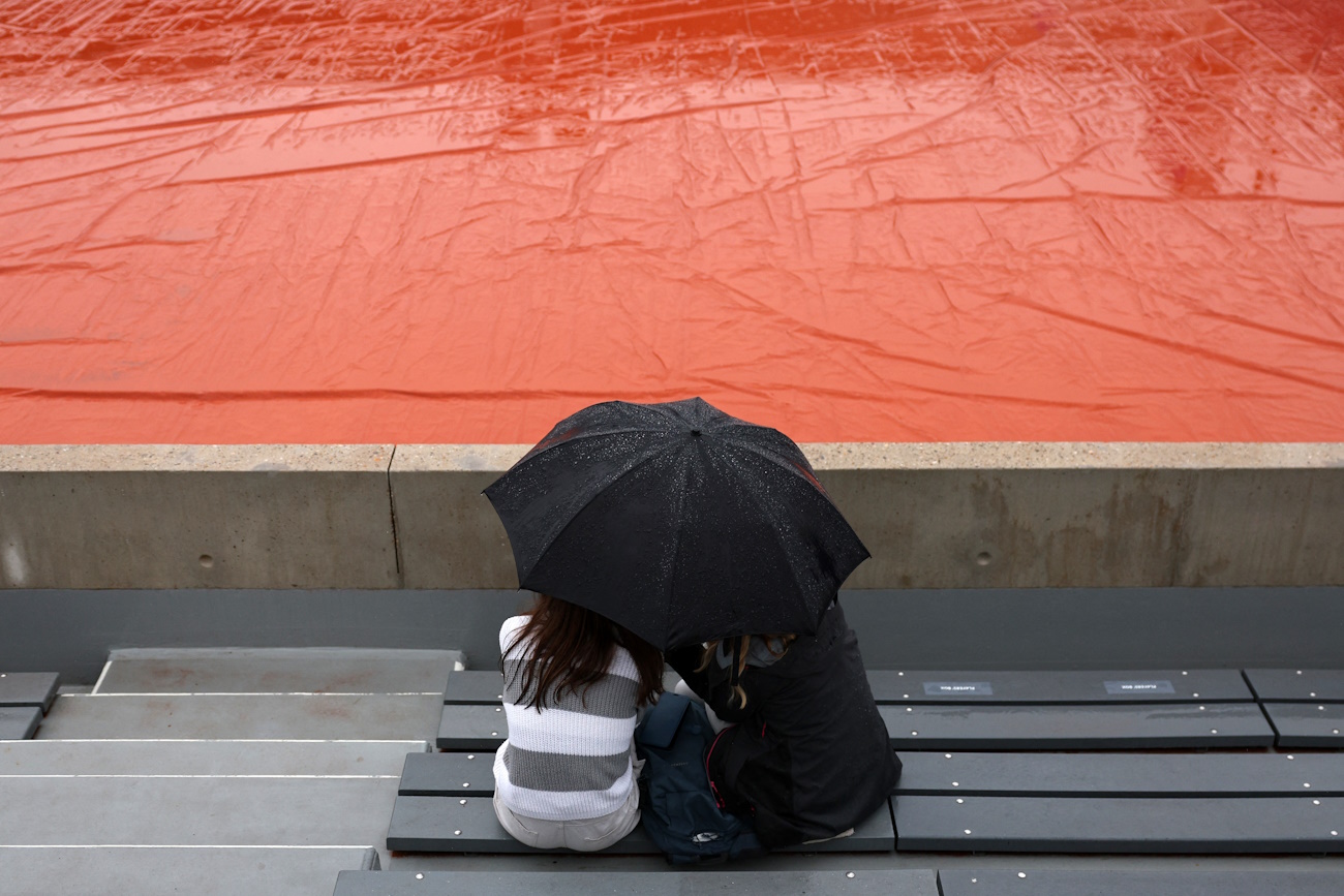 Paris 2024 Olympics - Tennis - Men's Singles First Round - Roland-Garros Stadium, Paris, France - July 27, 2024. Spectators sit under an umbrella as rain delays the match. REUTERS