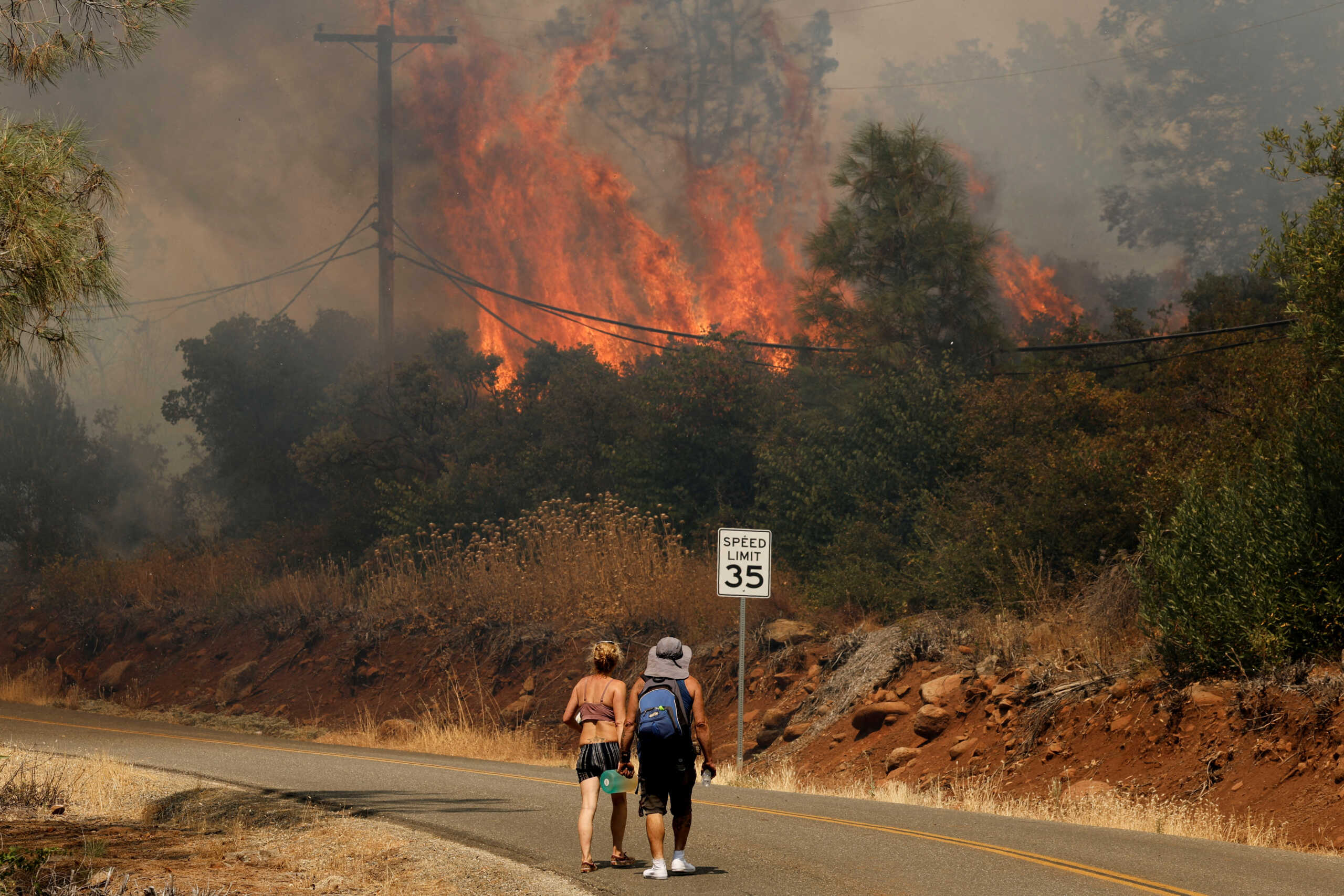 People walk on the road near flames and smoke plume rising as firefighters continue to tackle the Park Fire near the northern Sacramento Valley city of Chico, California, U.S. July 25, 2024.  REUTERS