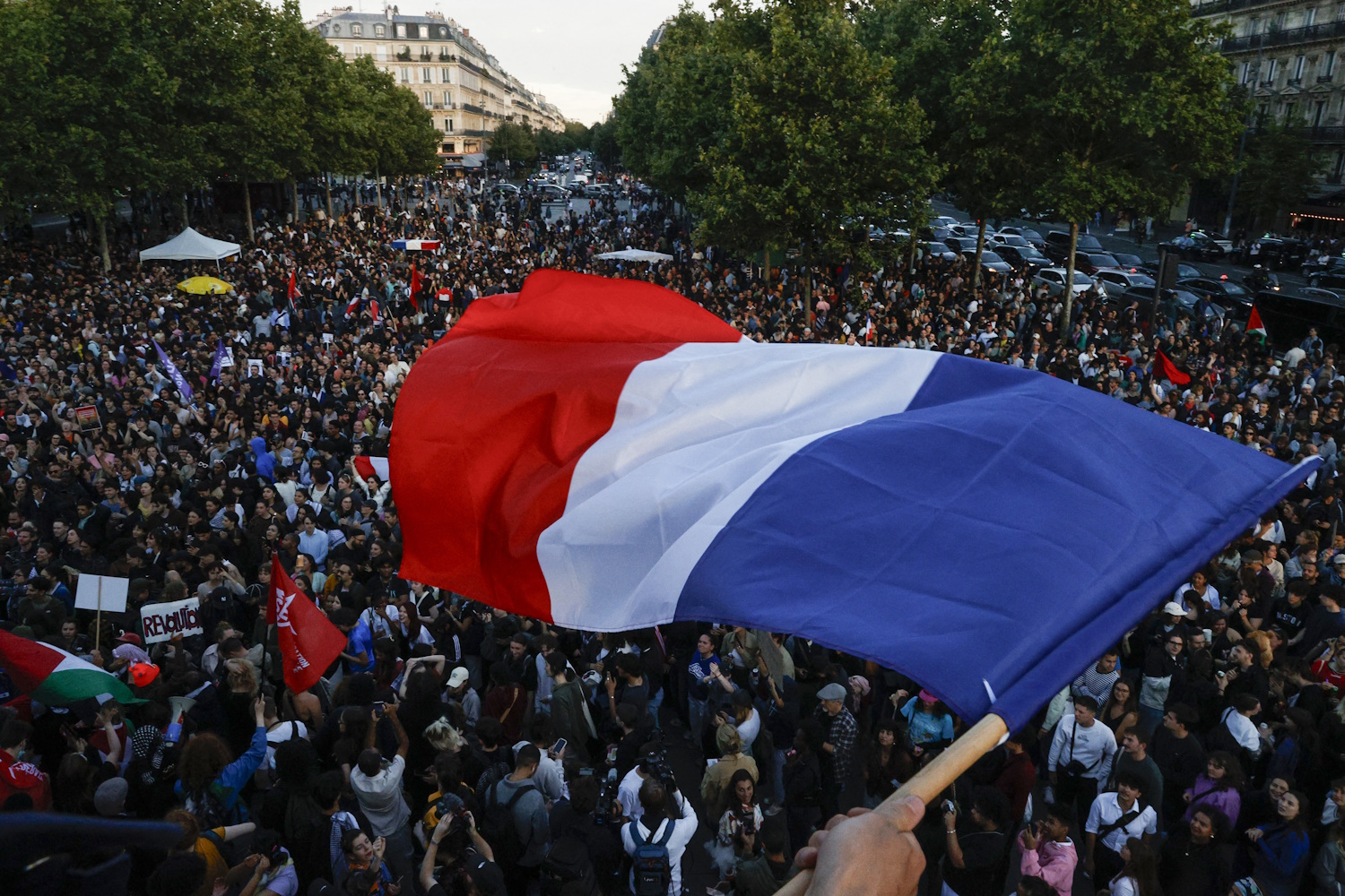 A protester hold a French flag as people gather at the Place de la Republique after partial results in the second round of the early French parliamentary elections, in Paris, France, July 7, 2024. REUTERS