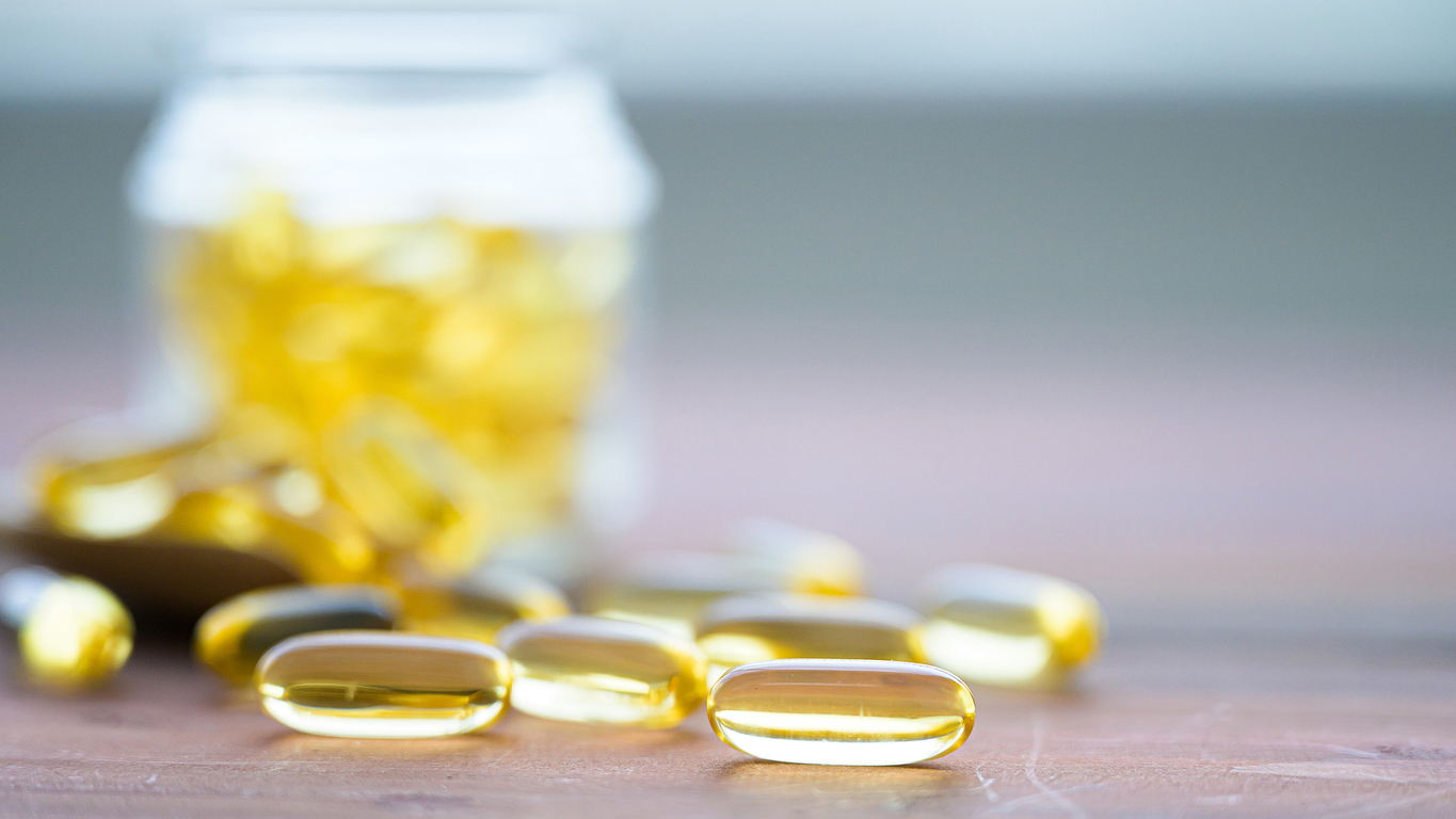 Pile of capsules Omega 3 in glass bottle on wood table