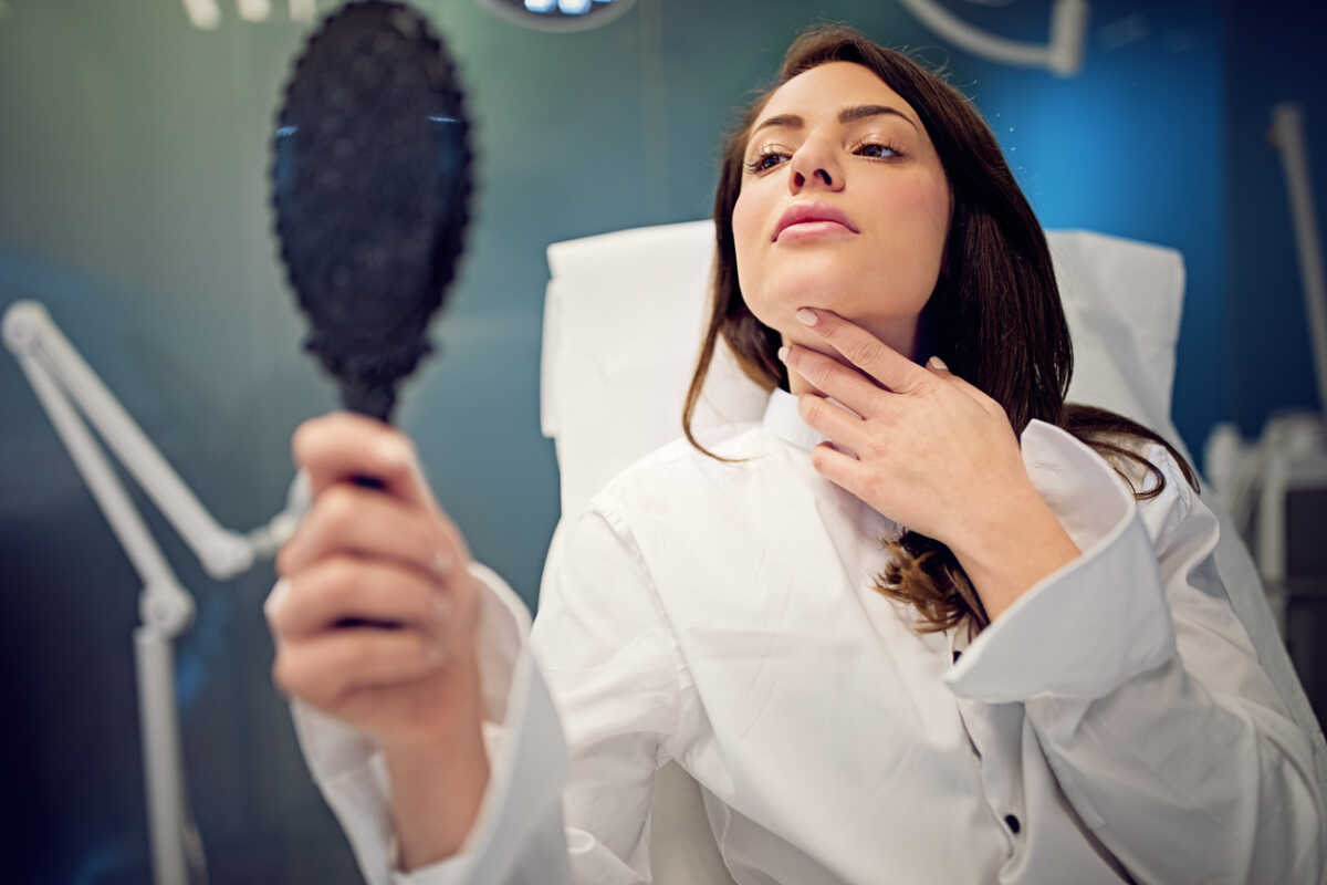 Young woman is looking her face in the mirror after beauty treatment procedure