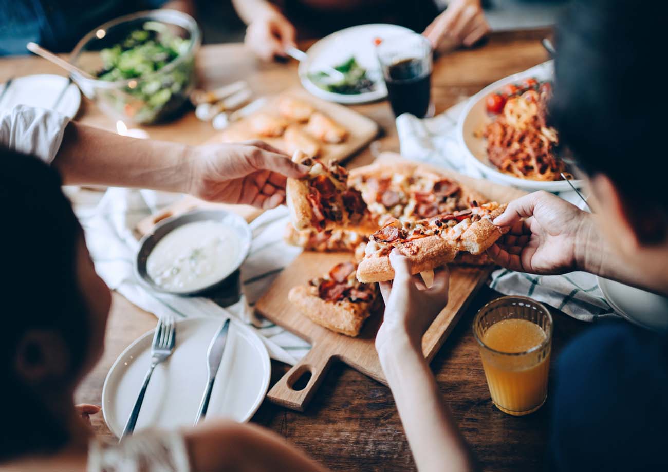 Close up of a young group of friends passing and serving food while enjoying together. They are having fun, chatting and feasting on food and drinks at dinner party