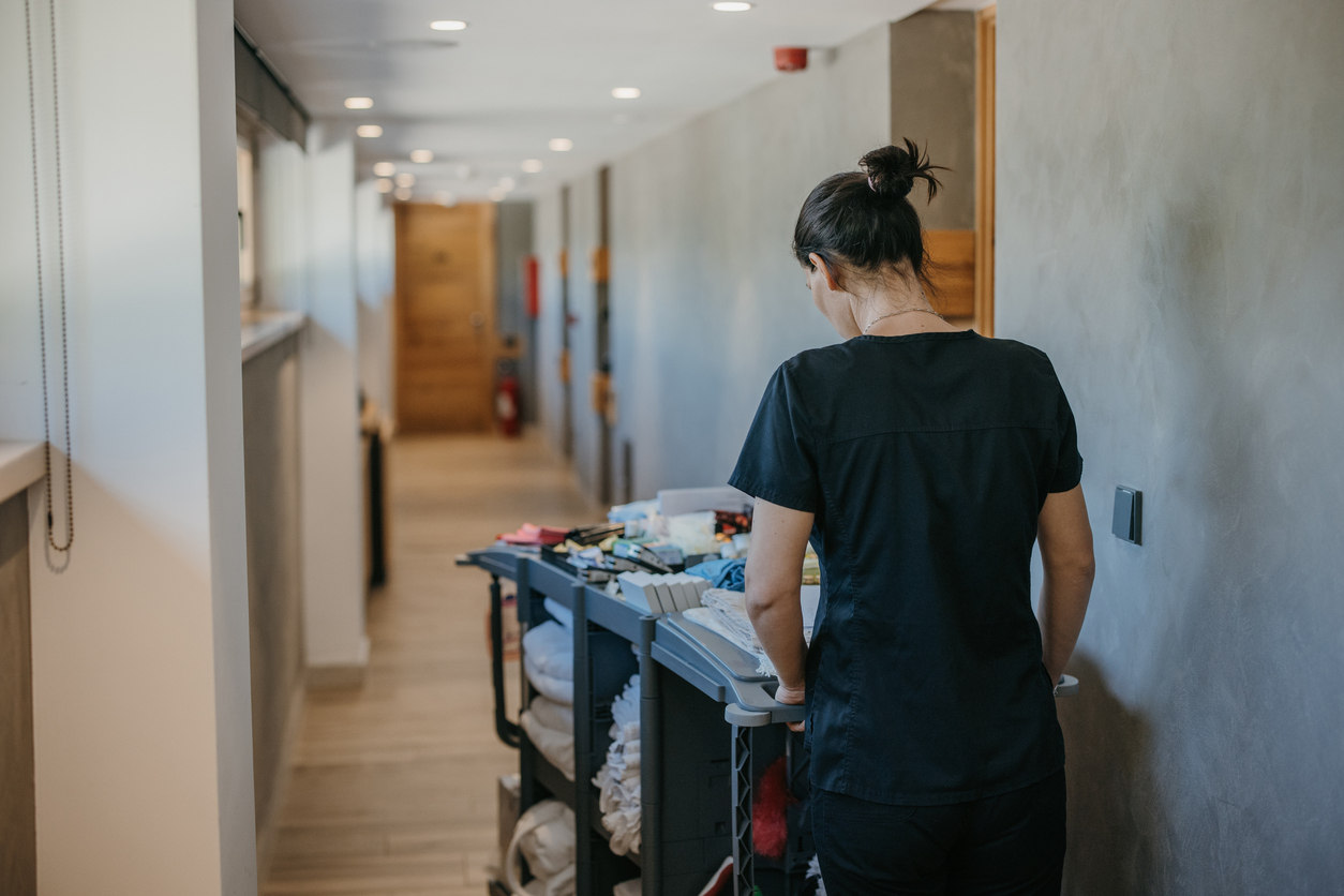 Young hotel maid in uniform pushing chambermaid trolley down the hotel corridor